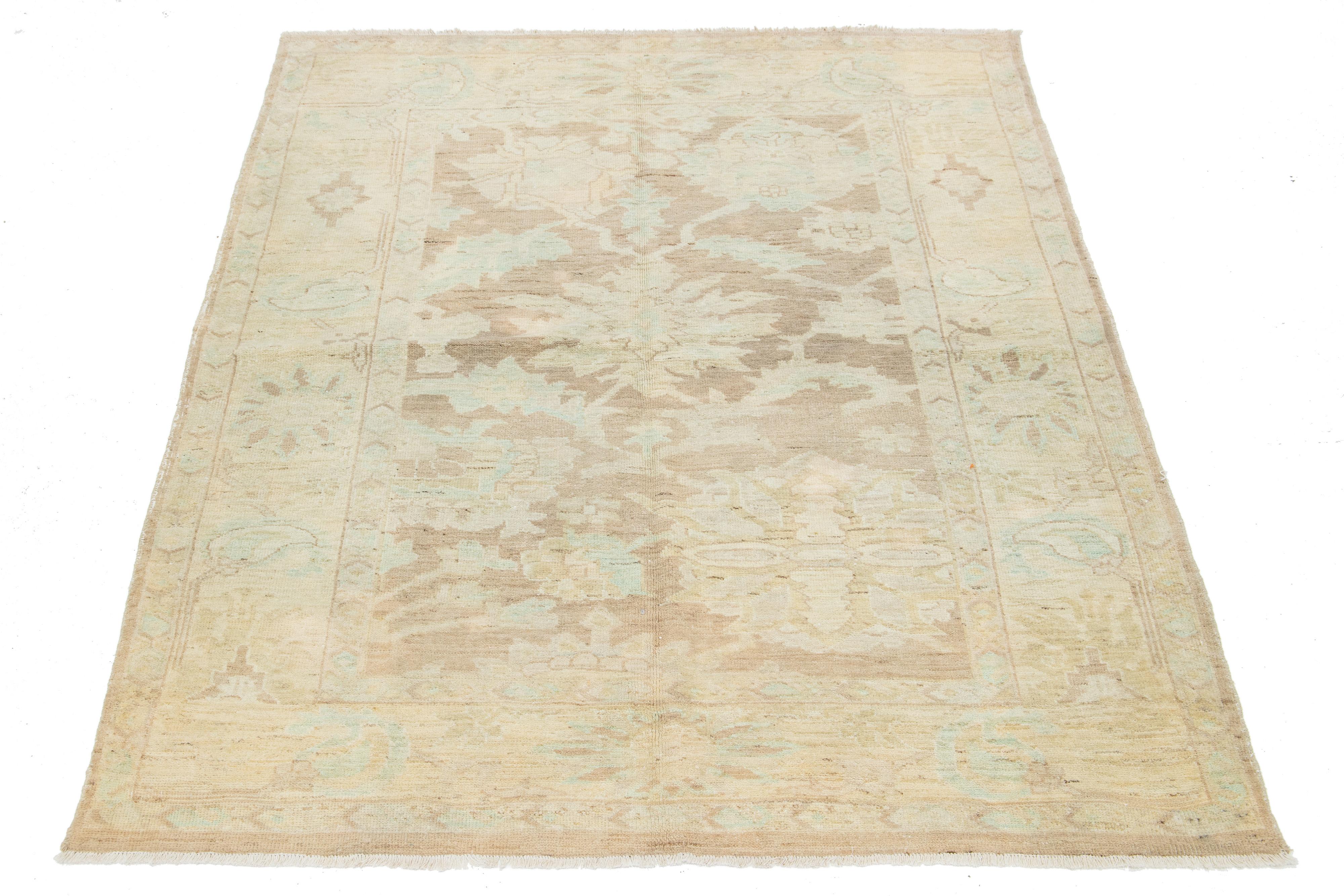 A hand-knotted wool rug featuring a light brown color field with a blue, beige, and green floral design.

This rug measures at 5'3