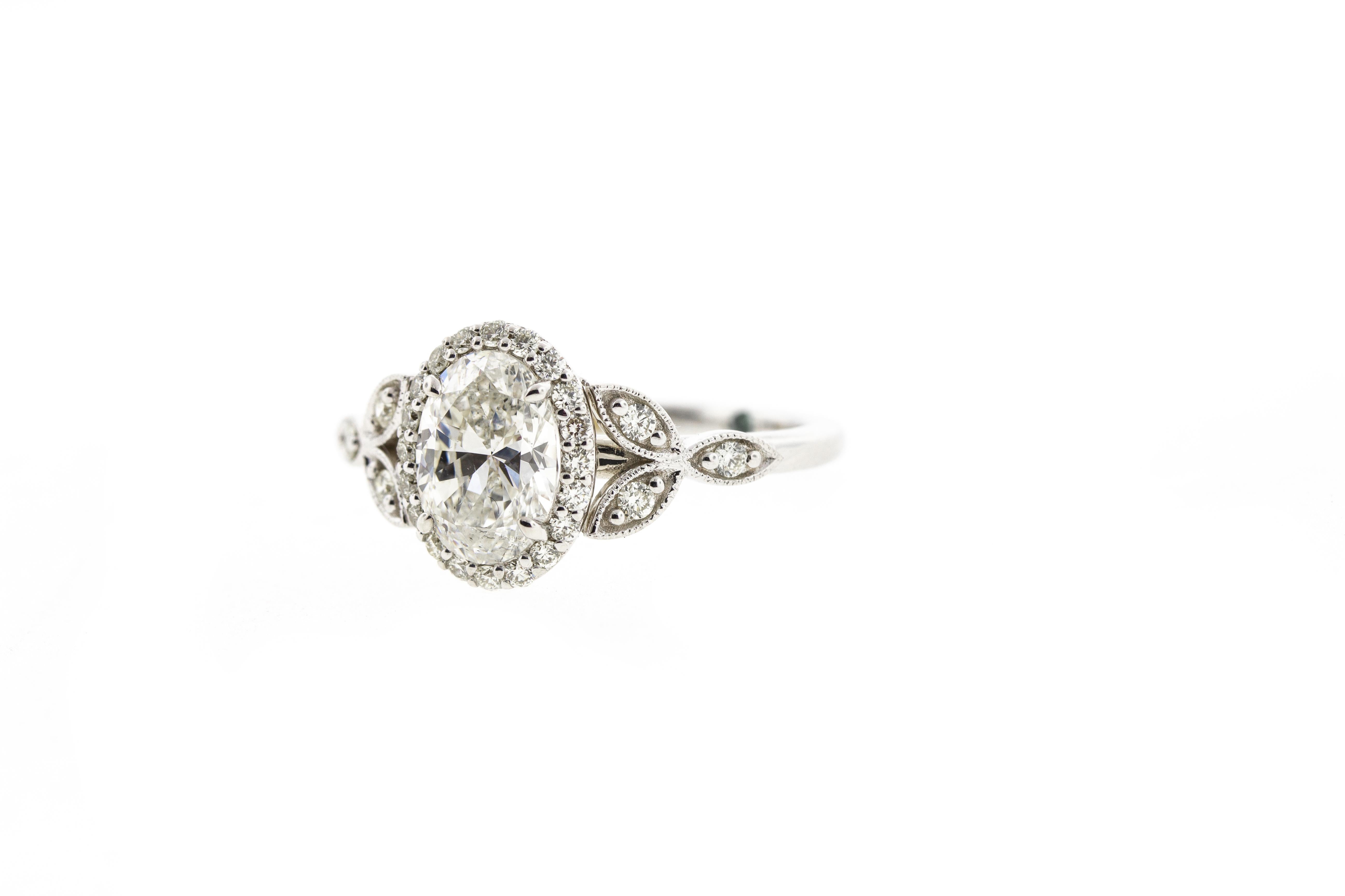 Unexpected and surprising detail abound with this delicate oval diamond engagement ring crafted in the Victorian style. A delicate balance of side diamonds and a diamond halo pull the entire look together. Hidden gemstones on the inside of the shank