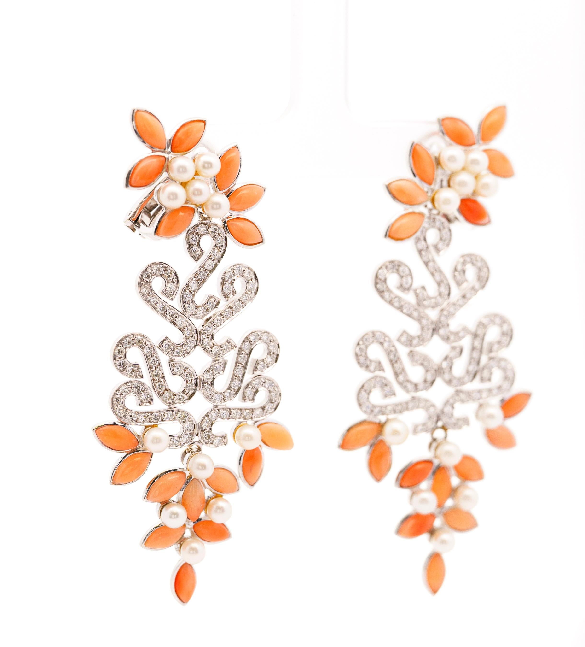 These captivating 3-inch earrings showcase a stunning floral design, crafted in lustrous 18k gold. Marquise-shaped coral pieces framing the sparkling round-cut diamonds, create a unique and eye-catching centerpiece. Delicate pearls add a touch of