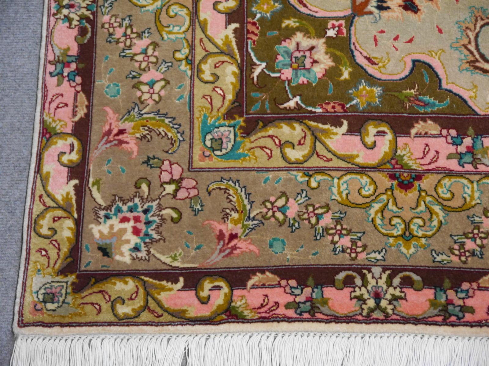 This breathtaking hand-knotted oriental rug was made of fine wool and pure, natural silk. It is very fine and has a stunning luster. The creme field contrasts with the olive green border and the pink motifs. The carpet has a lot of silk highlights