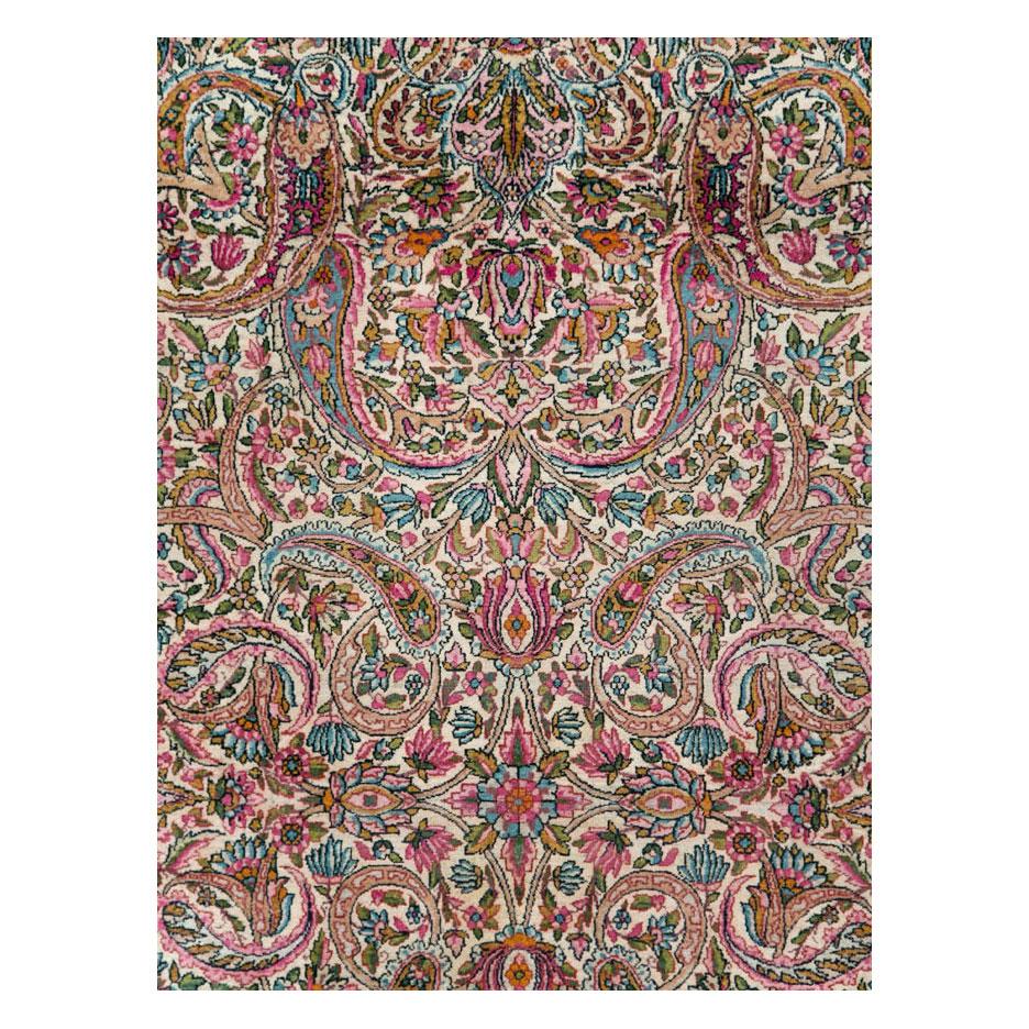 A vintage Persian Lavar Kerman room size rug handmade during the mid-20th century. The ivory field is filled with an intricate floral design consisting of various sized paisleys among other floral elements in colors including pink, blue, green, and