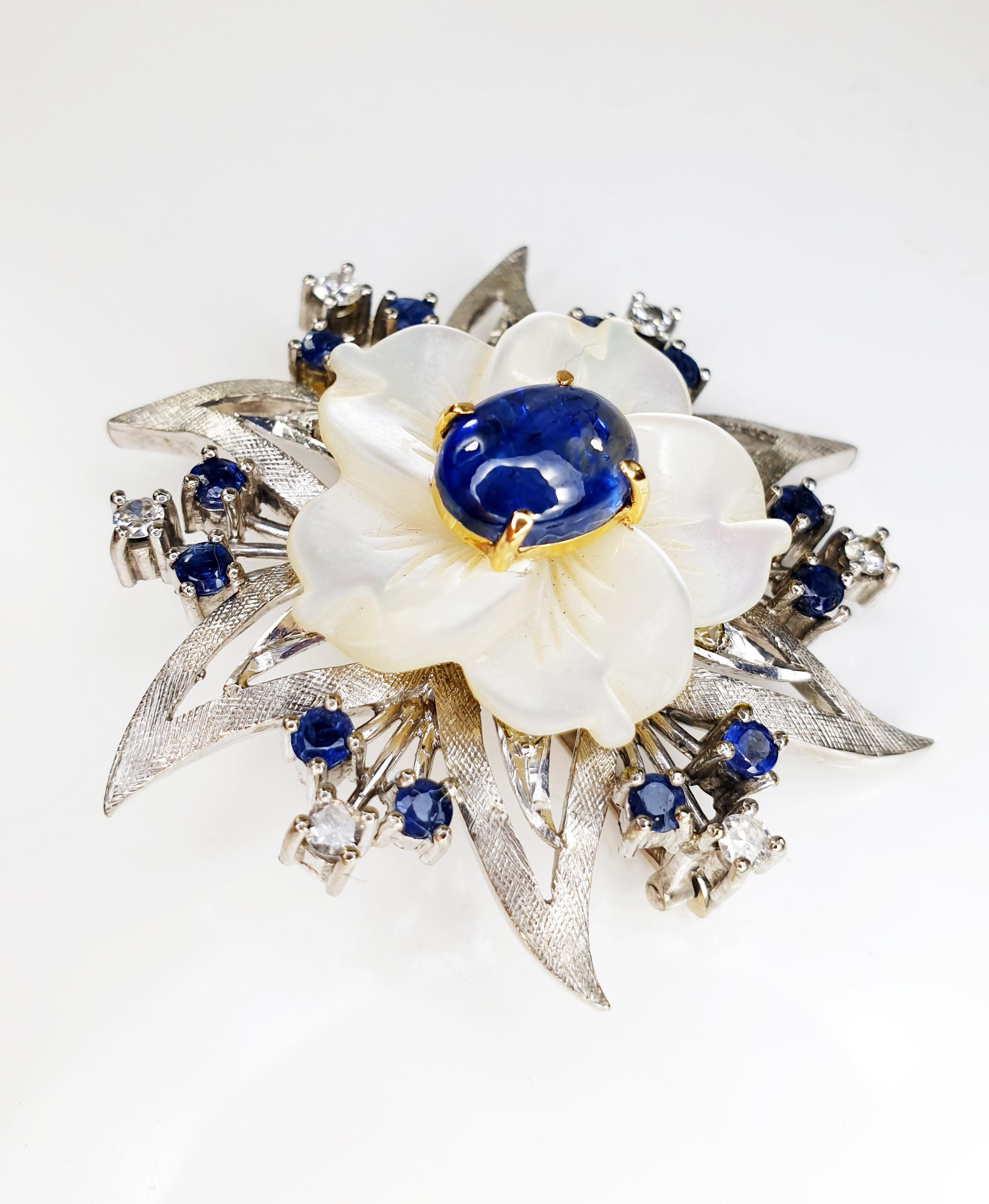 Fine and classic white 18kt gold brooche with 26 of 0.03ct diamonds total 0.78ct 
and mother of pearl flower with sapphire cabouchon center
6 diamonds of 0.03ct total 0.18ct and 
12 emeralds of 0.03  total 0.36 
Weight 14.3 grams 
Measures 4.4cm x