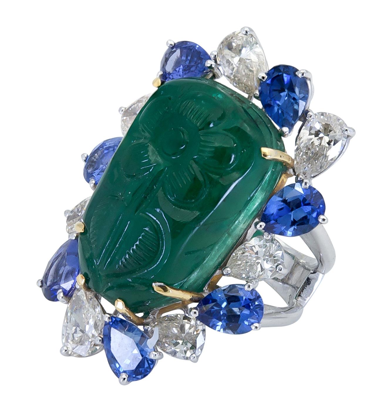 A unique cocktail ring showcasing a large green emerald carved with a potted flower. Surrounding the emerald are alternating pear shape blue sapphires and diamonds set in a polished mounting. 
Green emerald weighs 29.16 carats.
Blue sapphires weigh
