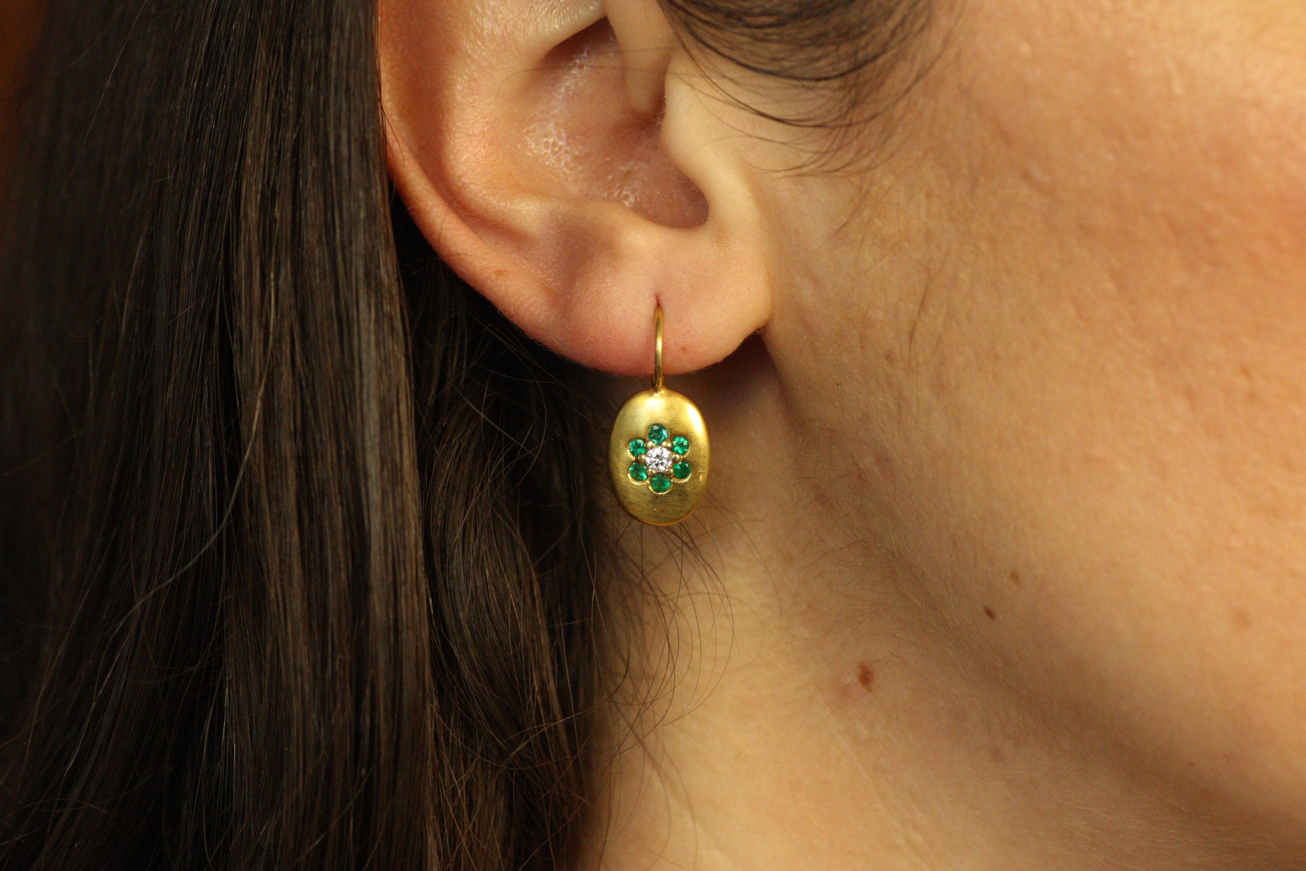 Ces élégantes boucles d'oreilles disque ovale fleuri présentent des émeraudes et des diamants éblouissants, sertis dans de l'or jaune 18 carats. Le design floral ajoute une touche fantaisiste et inspirée de la nature à ces boucles d'oreilles