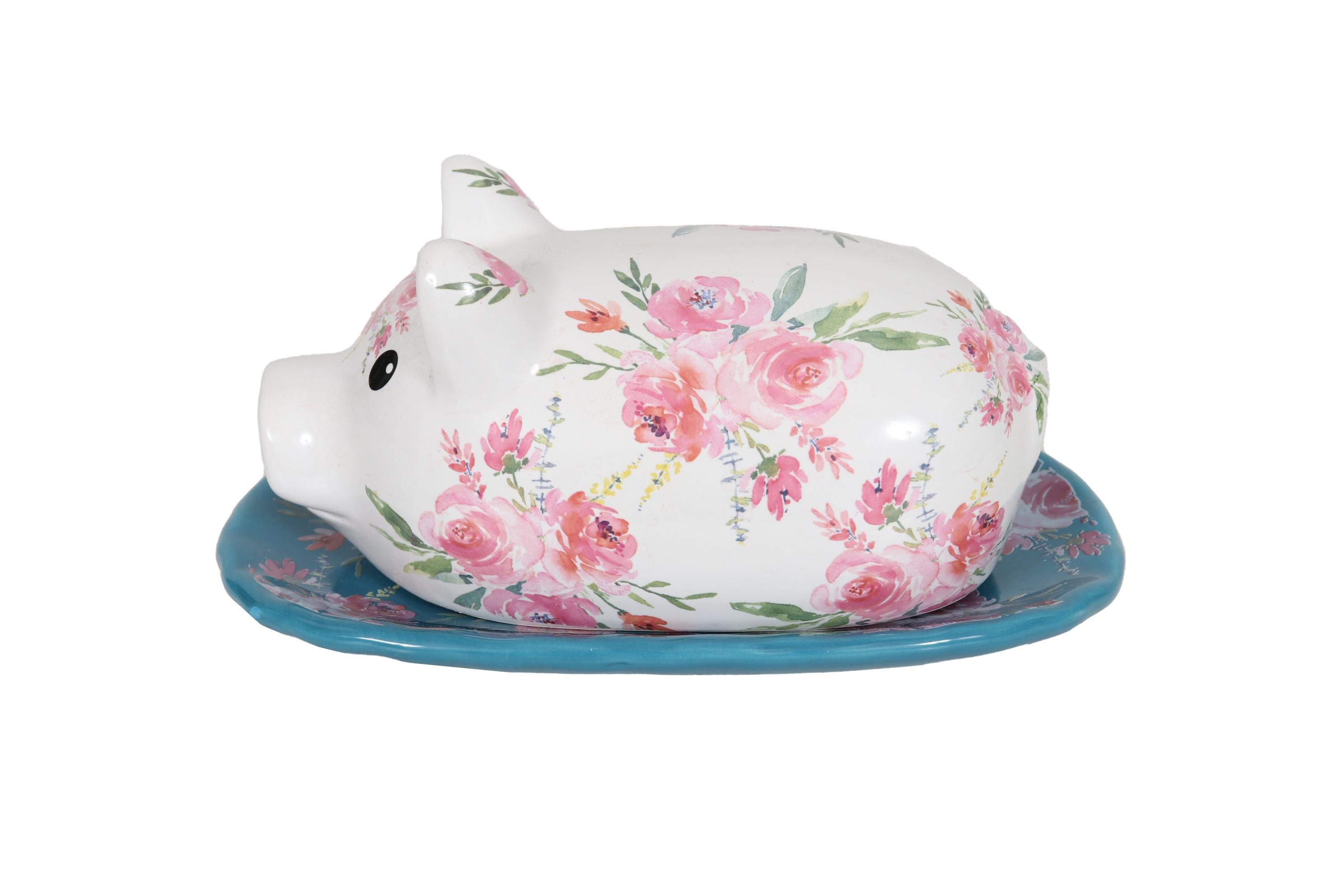 A floral ceramic transferware butterdish shaped like a pig. The lid is pressed with simple details to show the snout, ears and tail, and decorated with pink roses over a white background. The tray is blue and covered with matching pink roses.