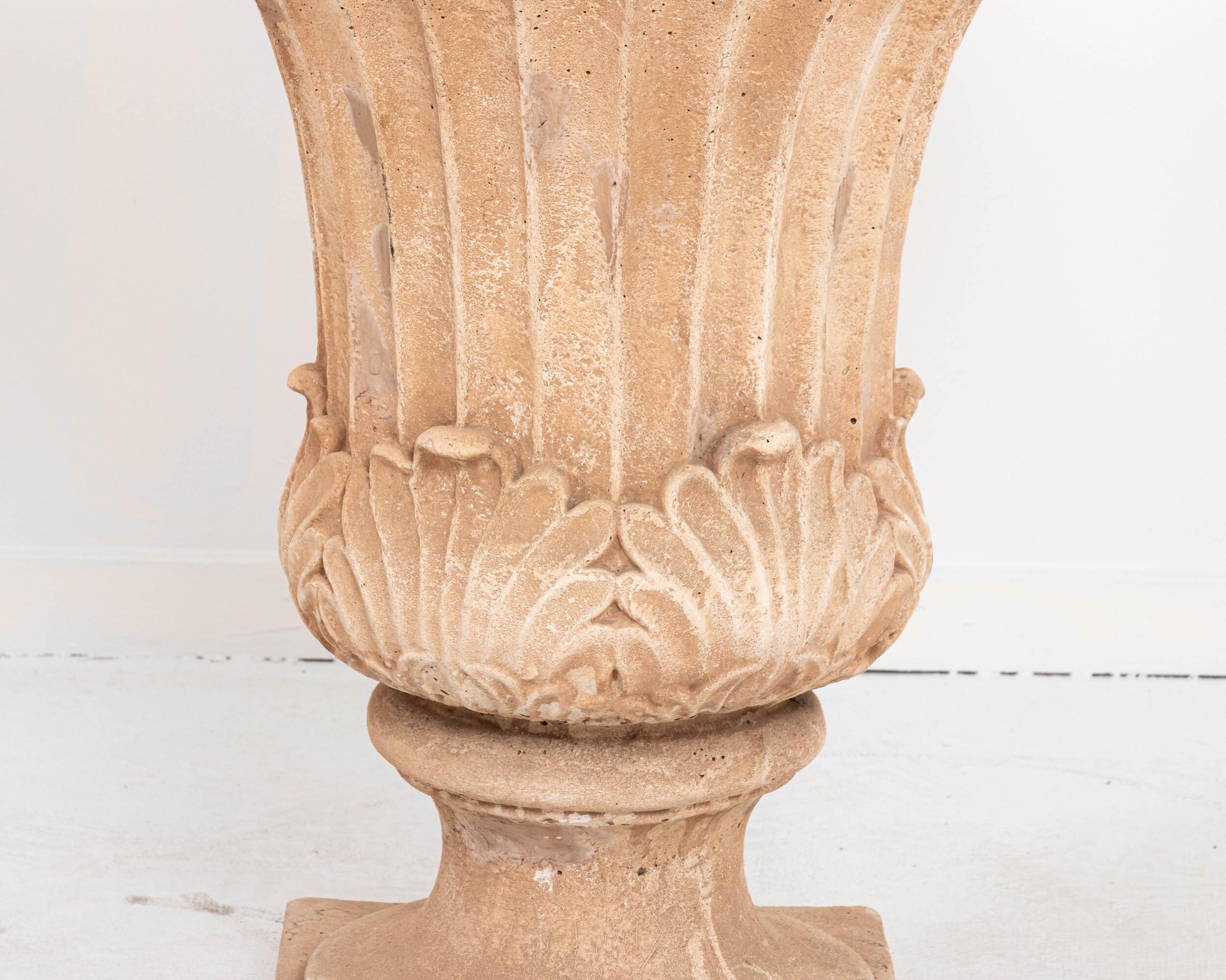 An open lily shaped cast iron and plaster covered garden urn. The plaster has been stained in a coral color. Square base. Wear consistent with age.