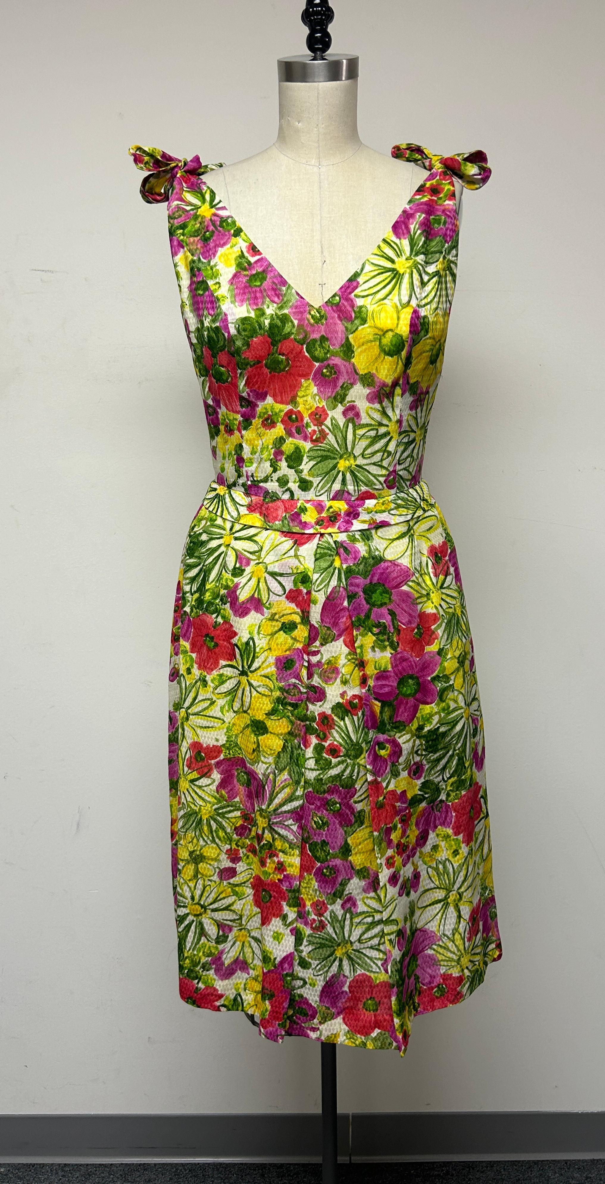 Mit lebhaftem, farbenfrohem Blumenmuster aus leuchtender Vintage-Baumwolle, gefüttert mit 100% Seide. Ein Sonnenkleid, das Ihre Stimmung an wärmeren Sommertagen heben wird.  
Die Silhouette mit den charmanten Schulterriemen, der Kellerfalte und dem