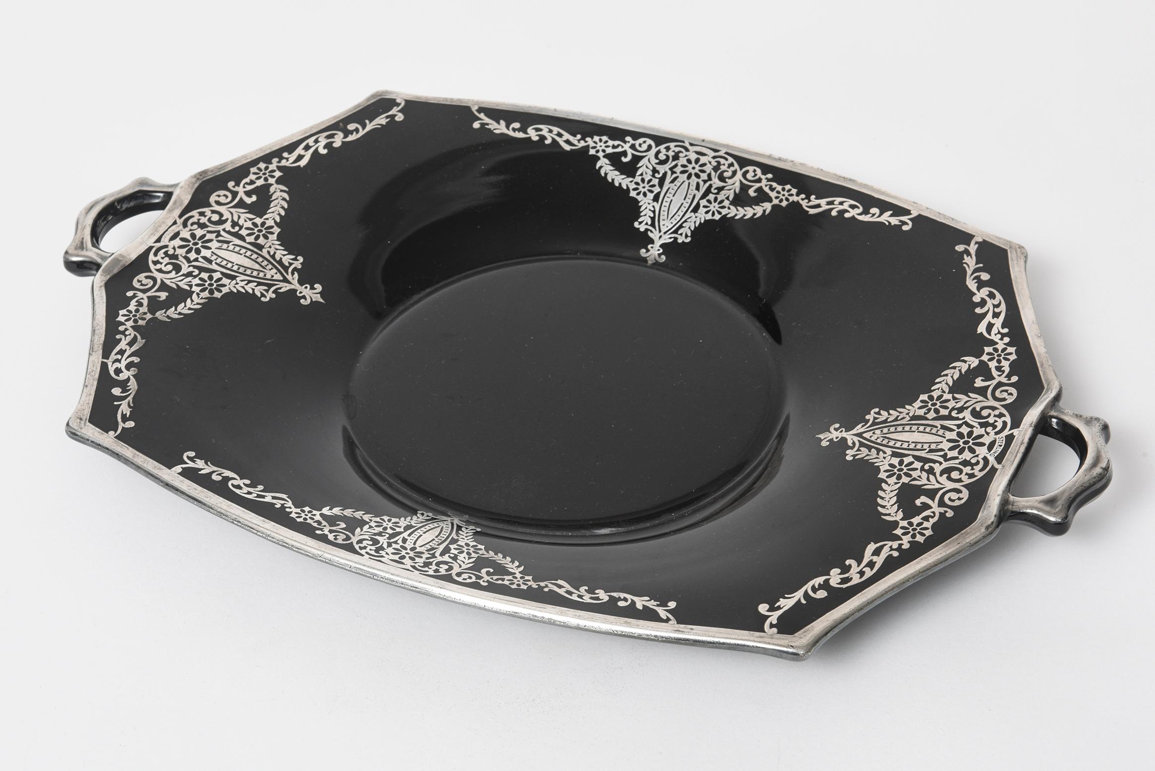 This shiny ebony black glass elongated octagonal serving tray features 4 sections with flowers, leaves and scrolls. The outer rim and the handles have a sterling silver line. Marked sterling in one of the designs by the handle. The tray levels down