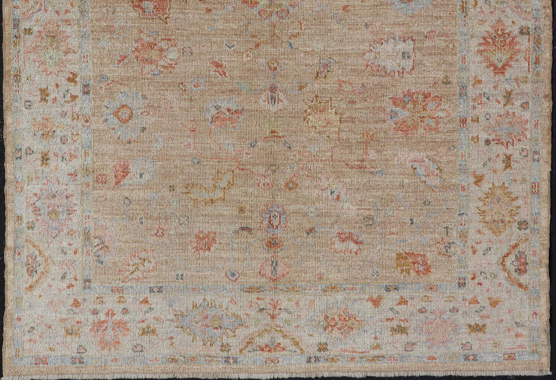 This Turkish Oushak was hand-knotted with angora wool. The field's background is rendered in a sandy-taupe, while the border's background is a cream color. The classic Oushak-floral design displays coral, salmon, maroon, olive green, and hints of