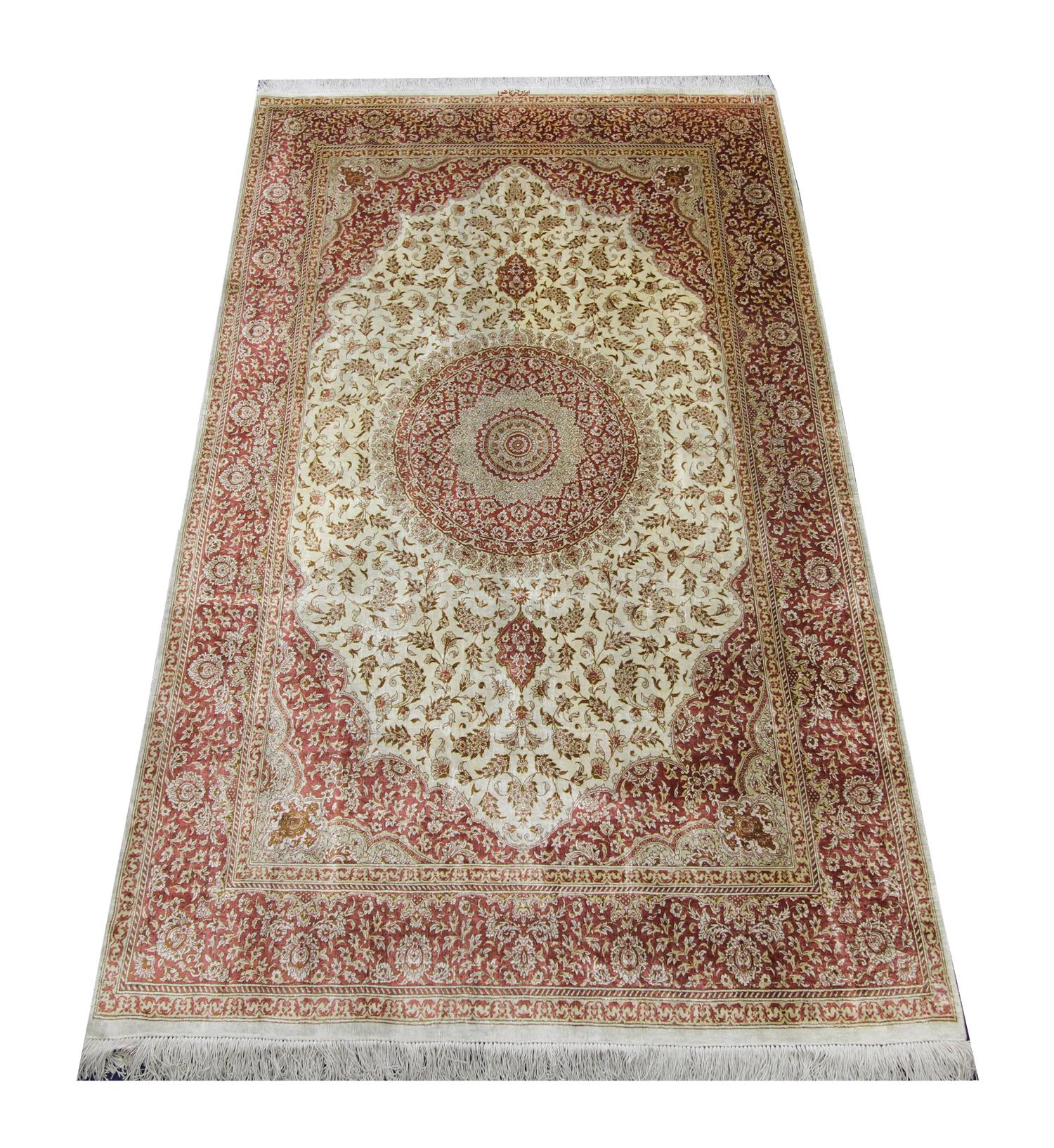 This elegant tribal silk rug was constructed in 1990 in Turkey. The central design features an ivory background with accents of red and beige that make up the symmetrical flowing design. This fine oriental rug combines simple colours with