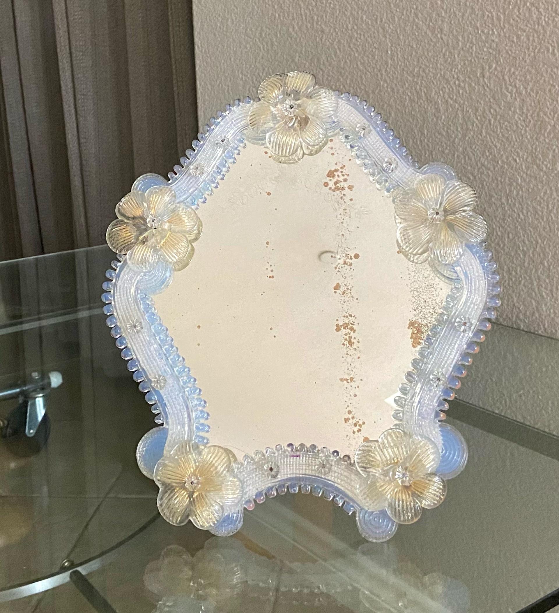 Murano vanity table mirror with clear and gold flowers, and opalescence color glass pieces surrounding the mirror. Mirror glass has decorative etching. The stand and backing are wood. 
 