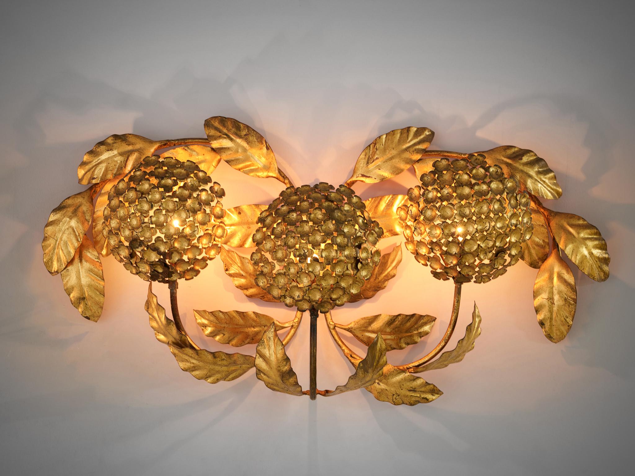 Floral wall light, brass, European, 1960s.

The lamp consists of three bulbs of flowers that diffuse the direct light. These bulbs protrude from the wall by their stems. The leaves that adorn the three bulbs get beautifully lit by the lamp, giving