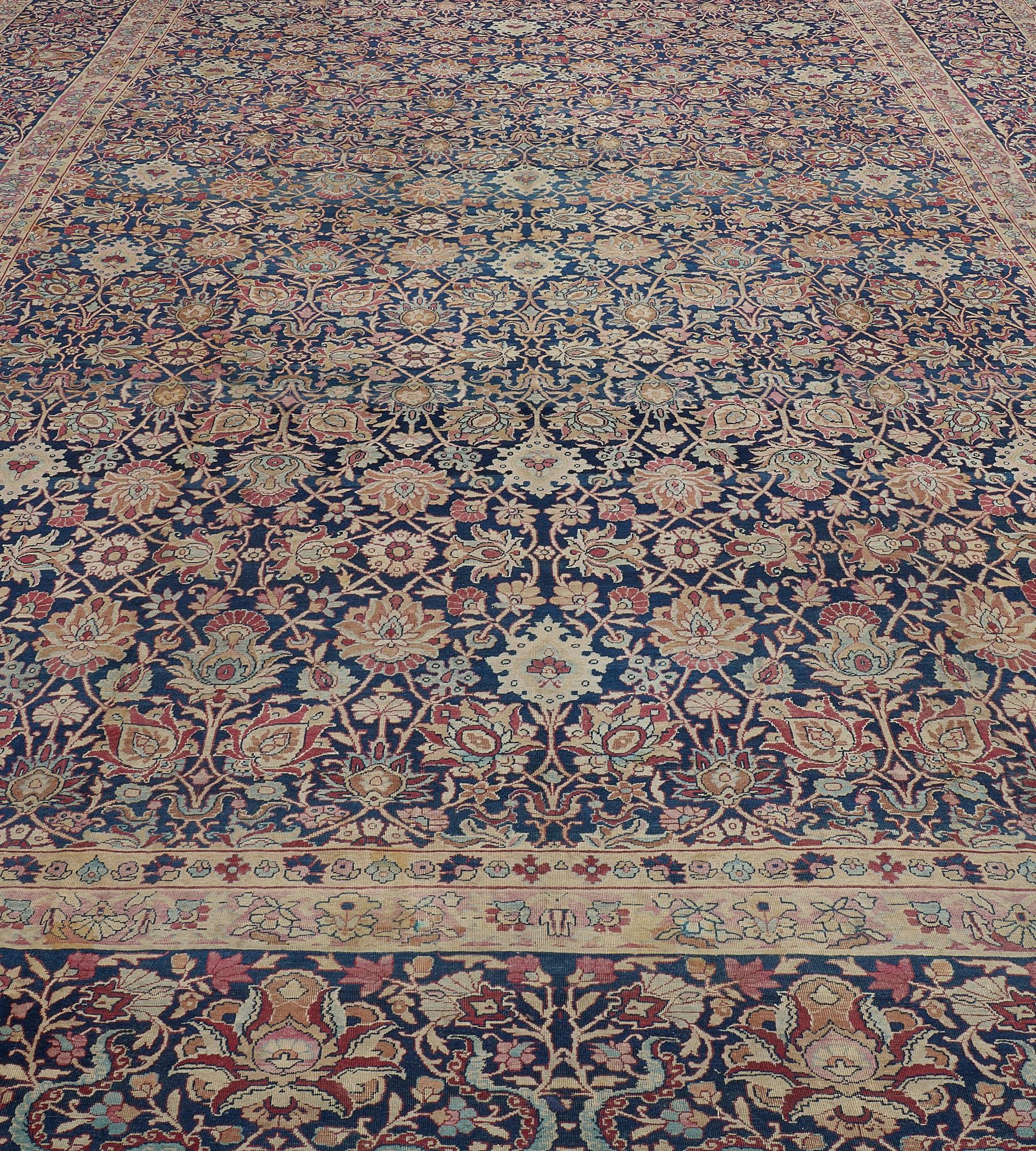This traditional hand-woven Persian Kerman rug has a deep indigo field of ornate palmettes issuing angled vine forming lozenge lattice, in a majestic indigo border of bold palmettes issuing detailed floral pattern, between magnificent ivory vine