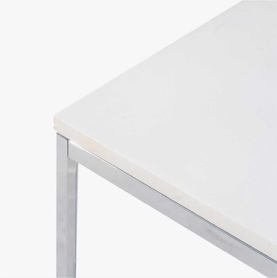 La table basse Florence Knoll, un élément de base du design, est présentée ici. Cette table a un beau plateau en pierre blanche avec un soupçon de veines gris clair. L'association de l'acier inoxydable poli et de la pierre blanche étant des plus