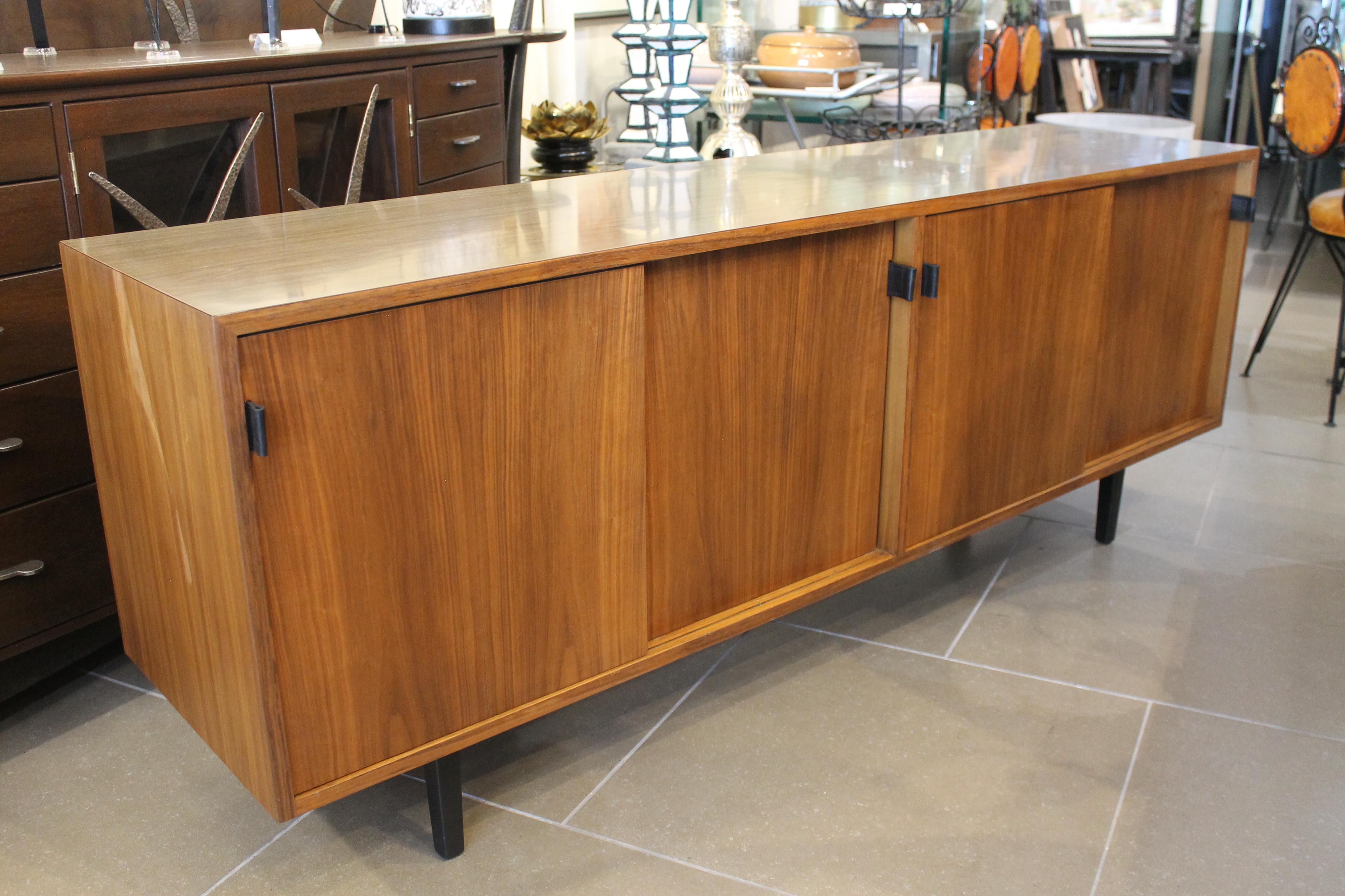 A Florence Knoll for Knoll Associates credenza, having a rectangular top above sliding doors with leather pulls and rising on tapered legs, with label verso. We replaced the leather pulls but, still have the original available.  We had the credenza