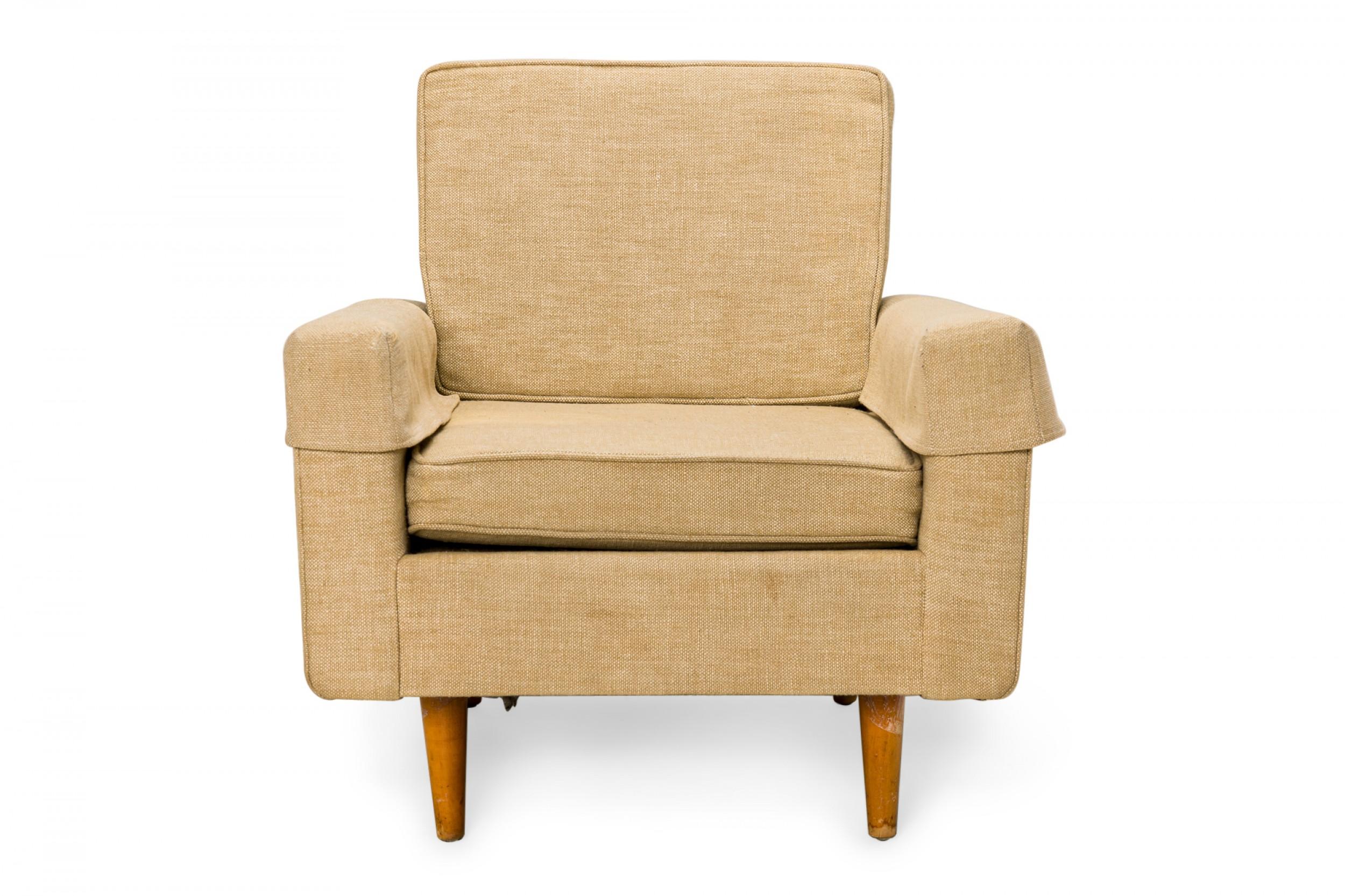 American mid-century lounge armchair with beige textured fabric upholstery and matching antimacassars, resting on four broad tapered wooden legs.(FLORENCE KNOLL FOR KNOLL INTERNATIONAL)