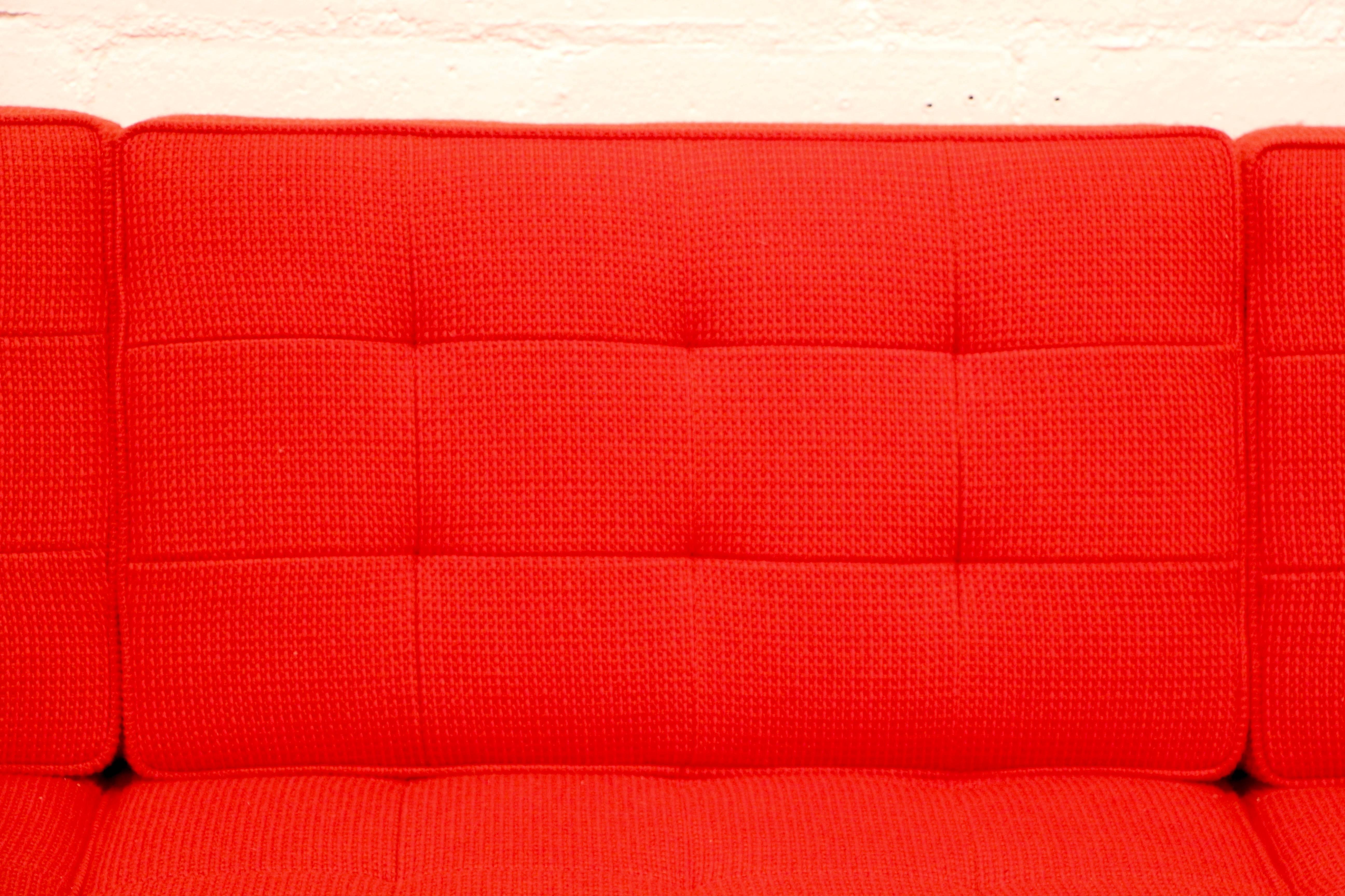 A nice of Florence Knoll sofa in Cato fire red fabric. They bear a tag that dates them to 2014. They were designed originally designed in 1954. The sofa has a little wear, showing some use. Marked on the leg as well Florence Knoll, Knoll Studios on