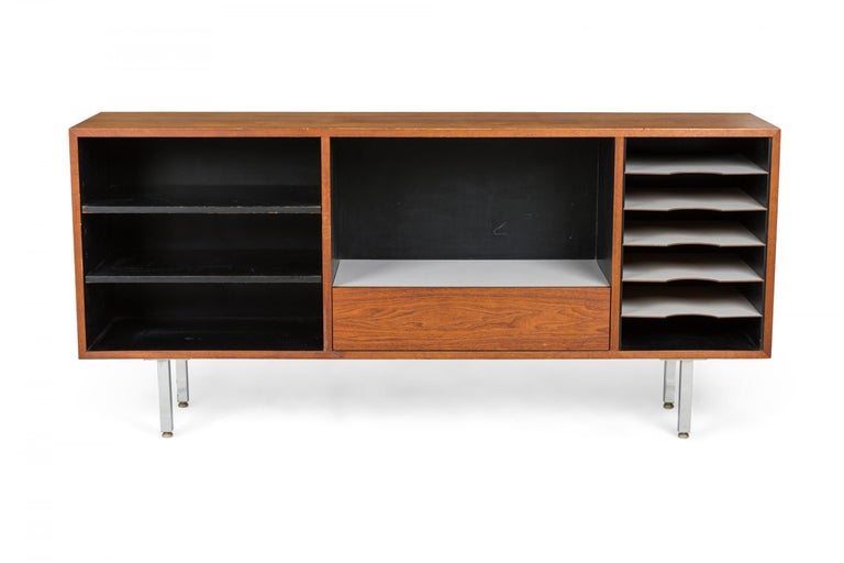 American Mid-Century storage cabinet / sideboard with open shelving compartments finished with black and white laminate in a walnut case with a single lower central walnut drawer, resting on four square chrome legs. (FLORENCE KNOLL / KNOLL