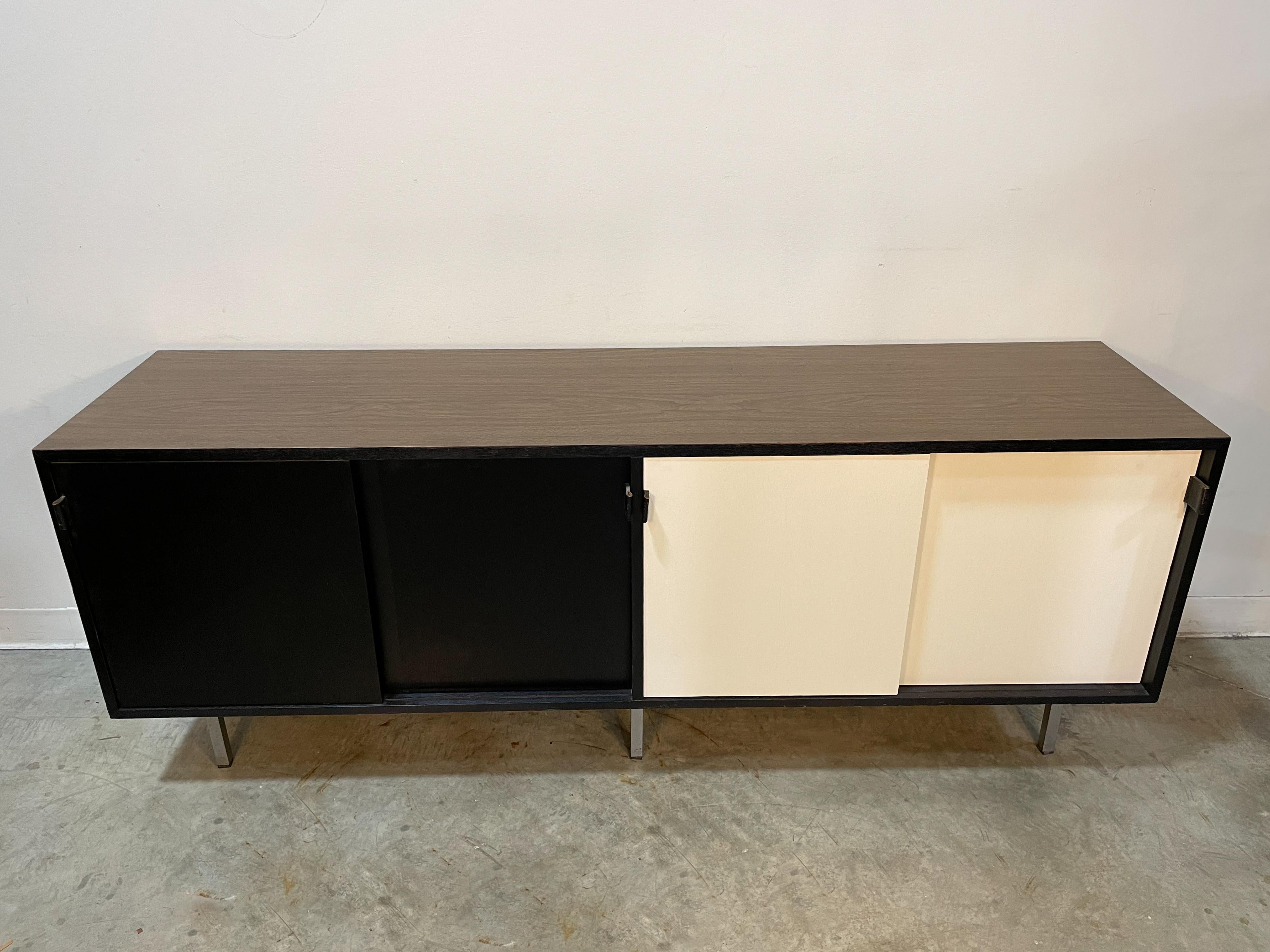 Mid-Century Modern credenza designed by Florence Knoll for Knoll circa 1957. Ample storage space with four adjustable shelves in an oak lined interior. Two-tone painted sliding doors with original leather pulls. Six chrome legs provide excellent