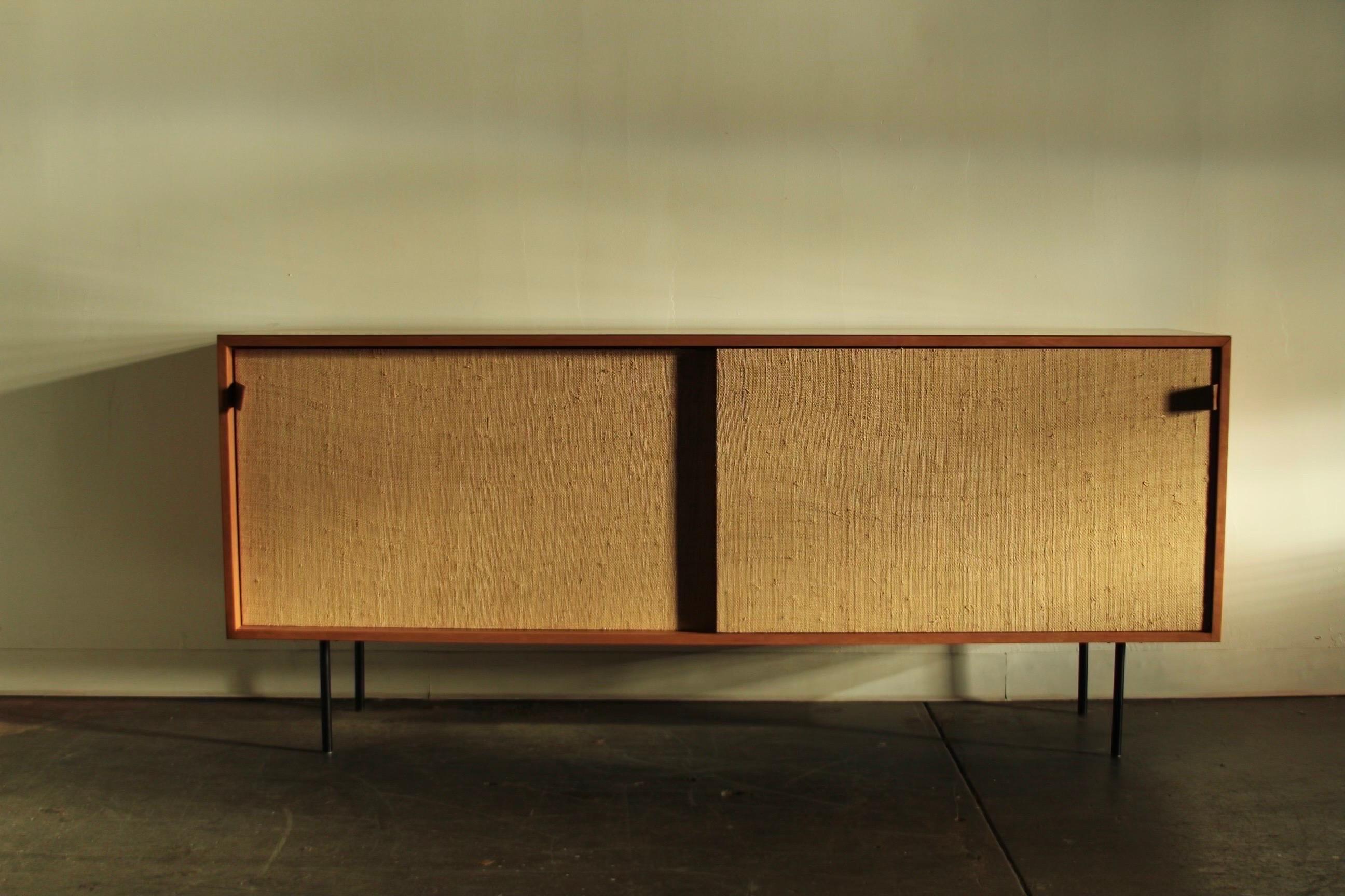 A maple, grasscloth and leather 'Model 116' cabinet designed by Florence Knoll in 1948 for Knoll Associates. The credenza features a pair of sliding doors with grasscloth fronts and stunning, hand stitched saddle leather handles, opening to a white