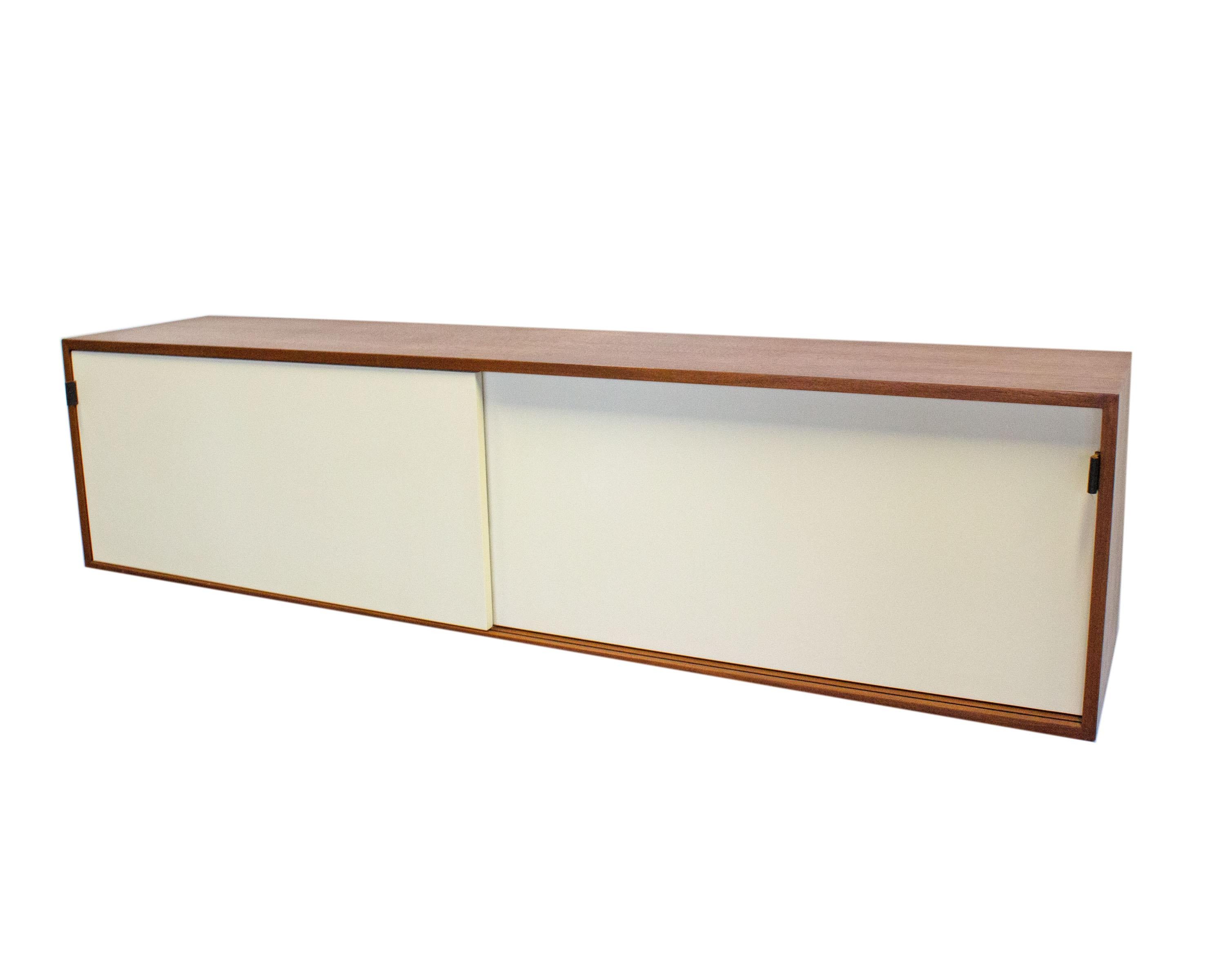 A model 121 W-1 wall mount credenza designed by American designer Florence Knoll (1917-2019) for Knoll International. The credenza has two sliding doors which open to reveal interior storage. The white doors feature the original saddle leather tab