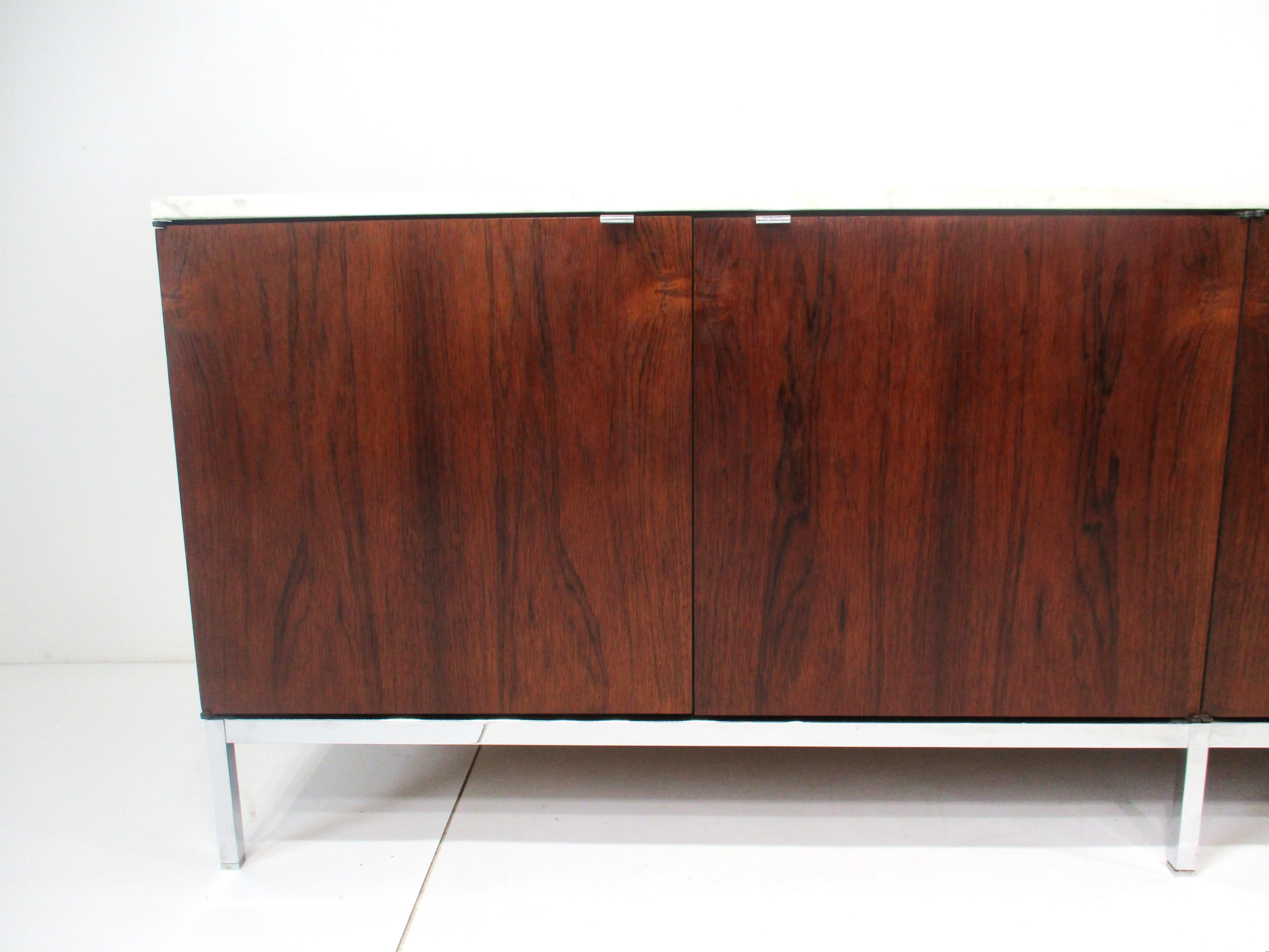 A nicely grained dark Brazilian rosewood credenza with white Carrara marble top having chrome legs , stretcher and pulls this four door credenza has contrasting clear oak interior and adjustable shelves . Designed by Florence Knoll for Knoll