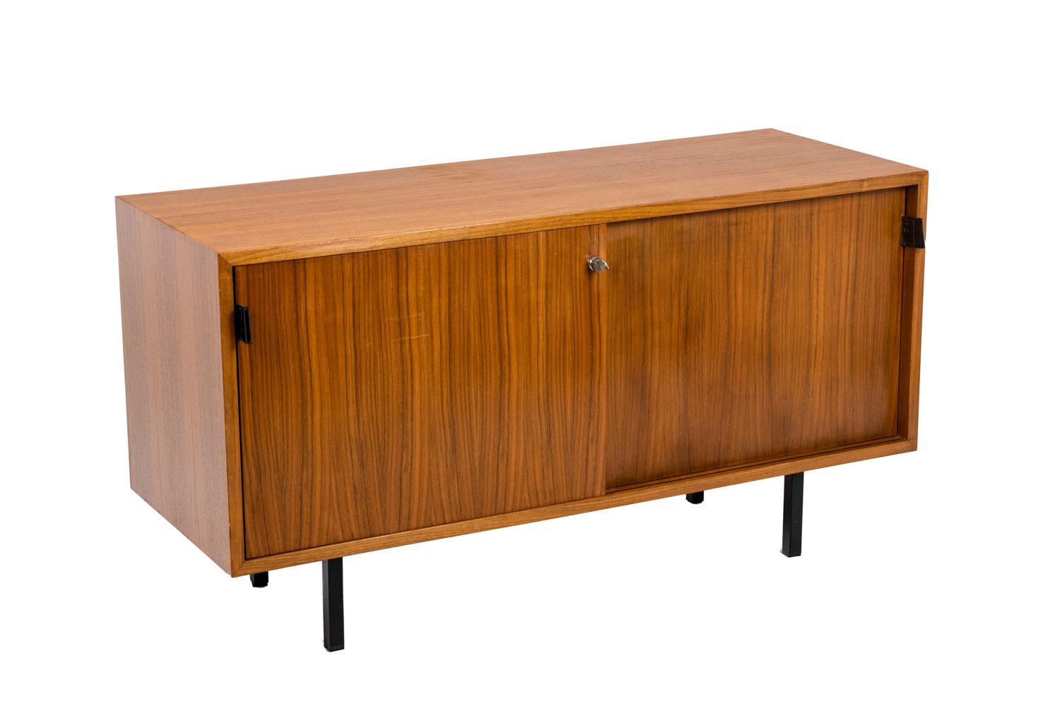 Florence Knoll, attributed to. 
Sideboard in teak opening with two sliding doors, standing on a four-legged square-section base in black tinted metal. Black leather handles. Two interior shelves. Original key.

American work realized in the