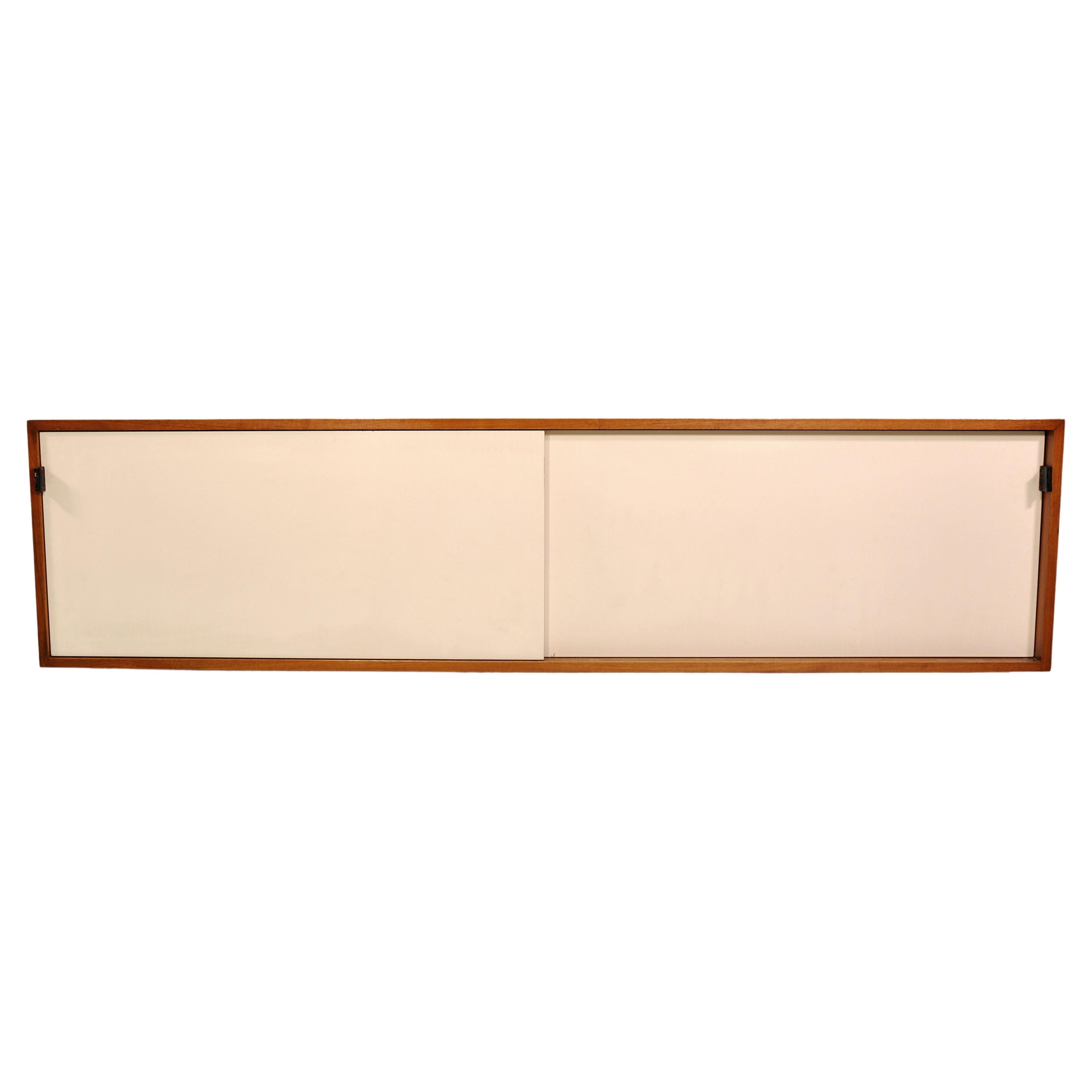 Early floating wall mounted cabinet model 123 W-1 by Florence Knoll for Knoll Inc. in walnut with lacquered wood interior. The hanging credenza features: two sliding doors; four compartments; original leather door pulls; original white lacquer