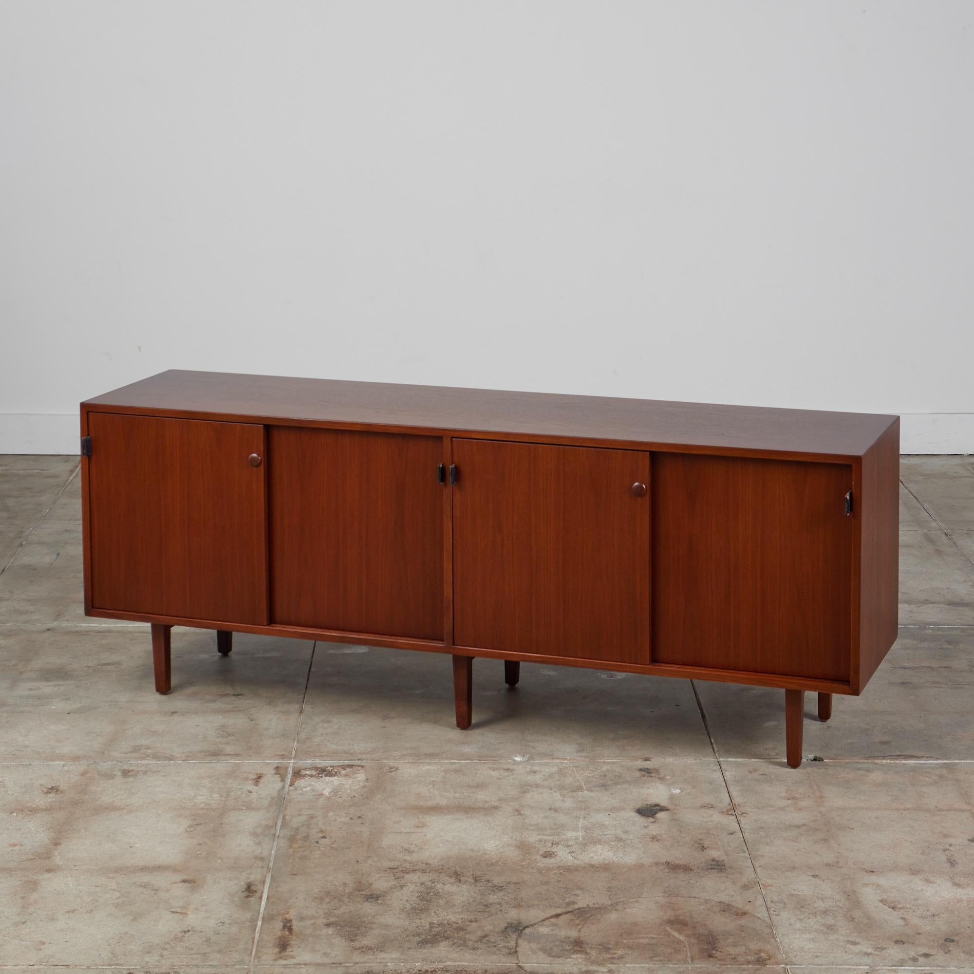 Four compartment early walnut credenza by Florence Knoll, USA, c.1950s. Three compartments features an oak interior with adjustable oak shelf and closes with sliding doors. A single compartment has a pull out drawer, perfect for filing or a record