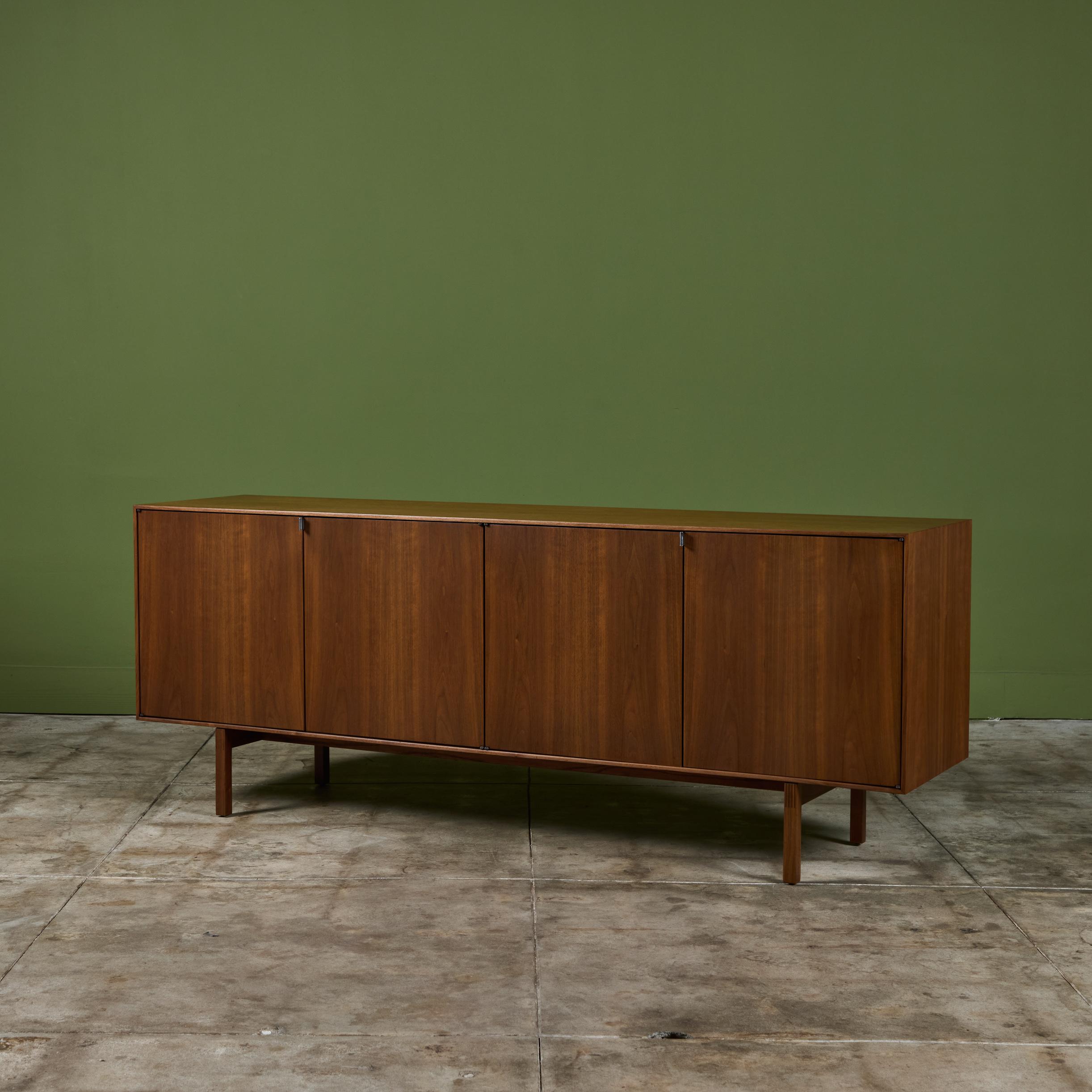 Two compartment early walnut credenza by Florence Knoll, USA, c.1950s. The piece features two hinged doors showcasing aluminum pulls. Each compartment features an oak interior, one with two drawers and two adjustable shelves while the other side
