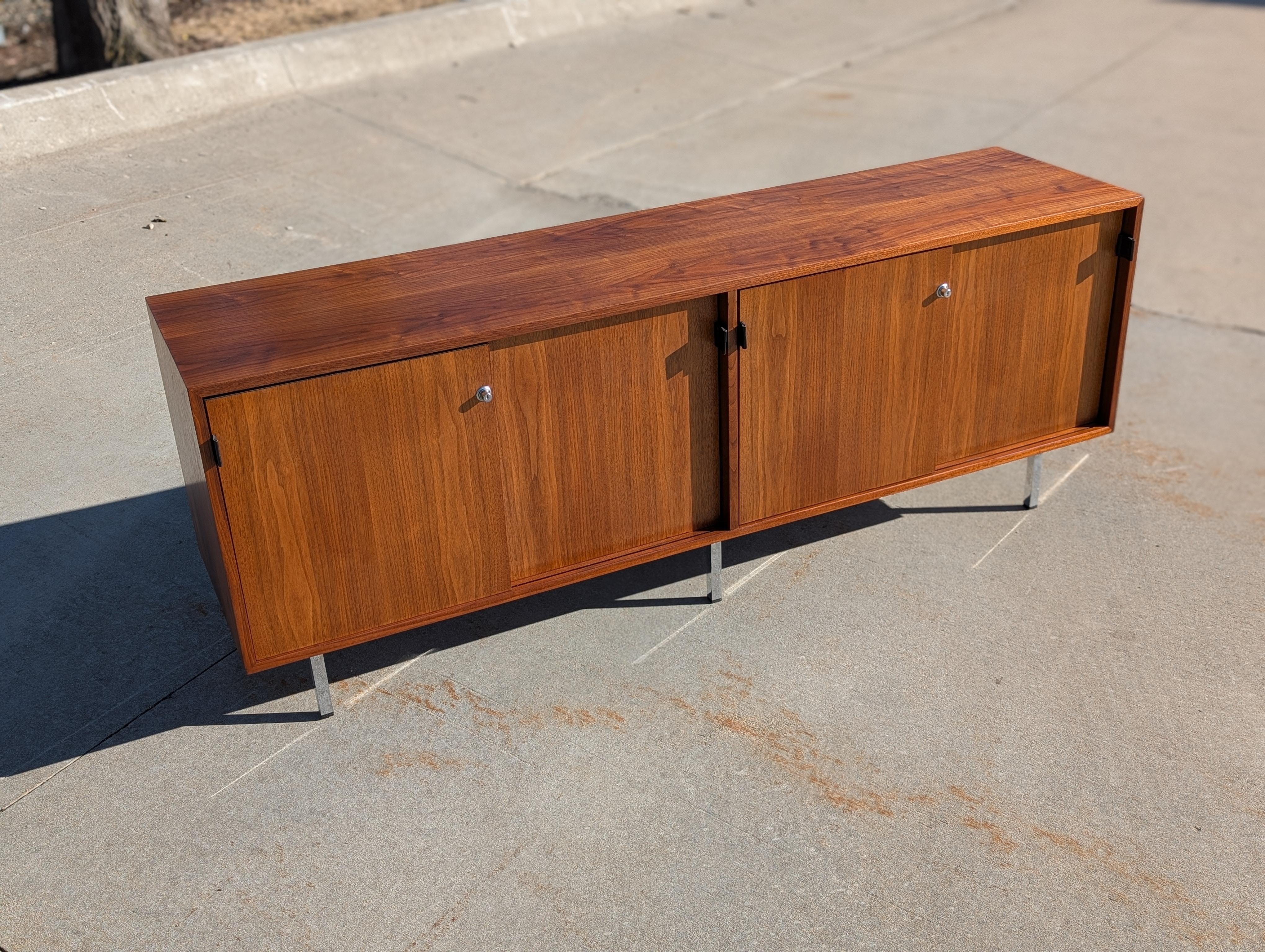 Walnut and white oak credenza with leather pulls, designed by Florence Knoll for Knoll International, circa 1970.

Exceptional walnut color, figure, and grain.

Four walnut sliding doors with black leather pulls open to four compartments. 2 large