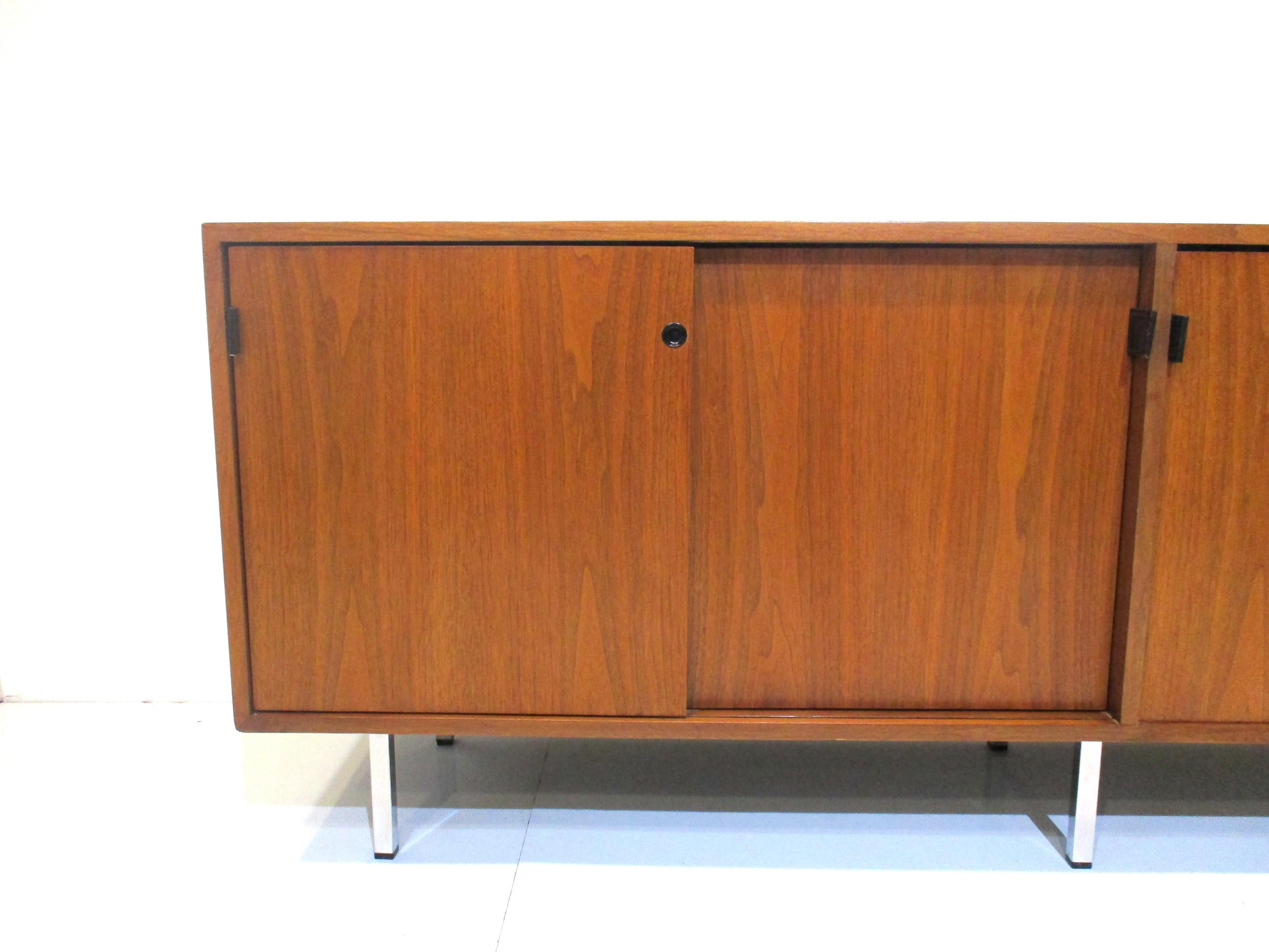 A very well crafted walnut credenza / sideboard with four sliding doors revealing three sections with adjustable shelves and one with four drawers all in a lighter oak tone giving the piece some drama . Black leather pulls open each door all sitting