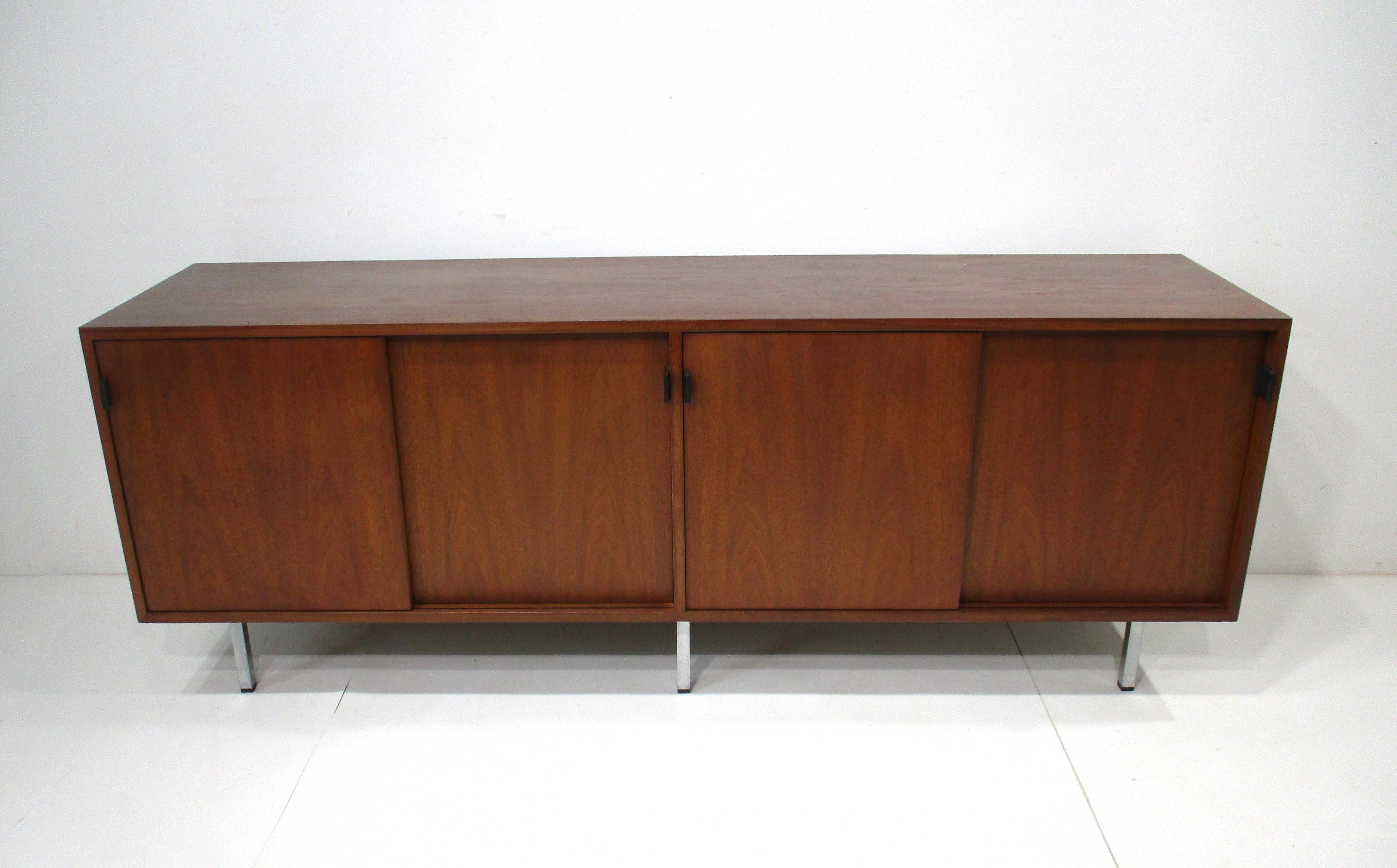 A very well crafted walnut credenza / sideboard with four sliding doors revealing four sections in contrasting clear oak with adjustable shelves giving the piece some drama plus functionally . Black leather pulls open each door all sitting on