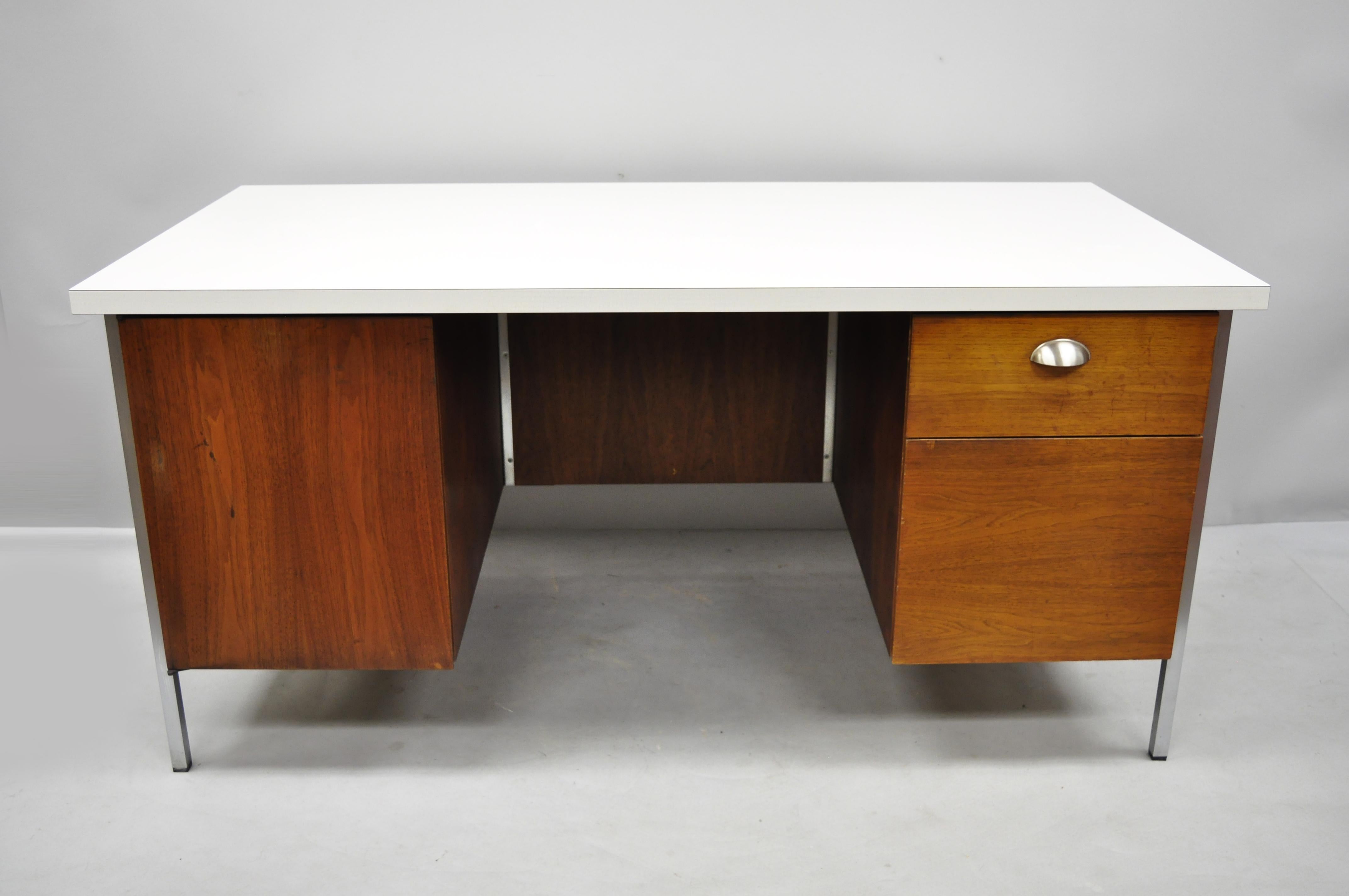 Florence knoll walnut executive desk with laminate top. Item features chrome frame, white laminate top, 2 drawers, 1 swing door, beautiful wood grain, finished back, original label. Measurements: 29