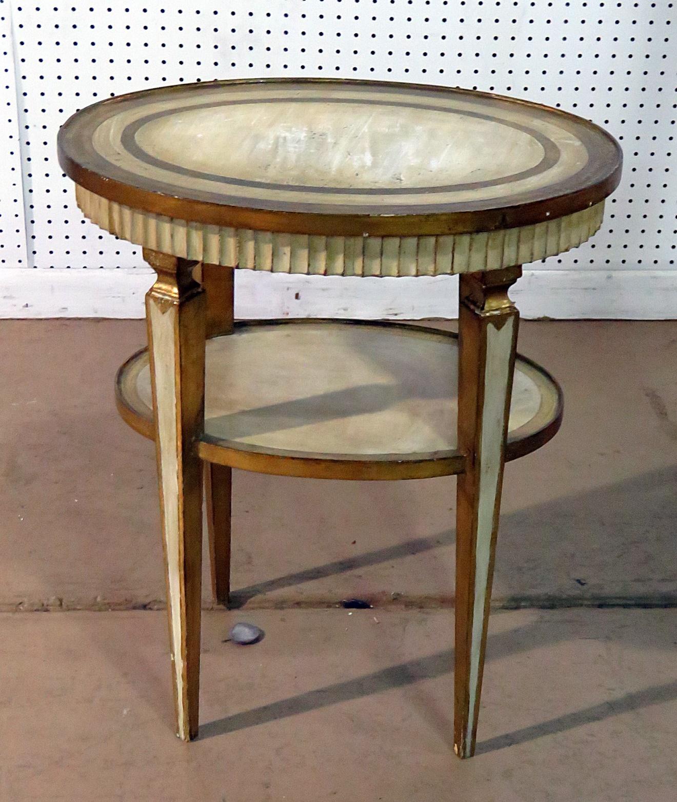 This is a very sophisticated Italian or Florentine 2-tier distressed painted side table with gilt decor. This table features beautiful antique creme painted surfaces and distressed genuine gold gilded surfaces too. Pay attention to the profile of