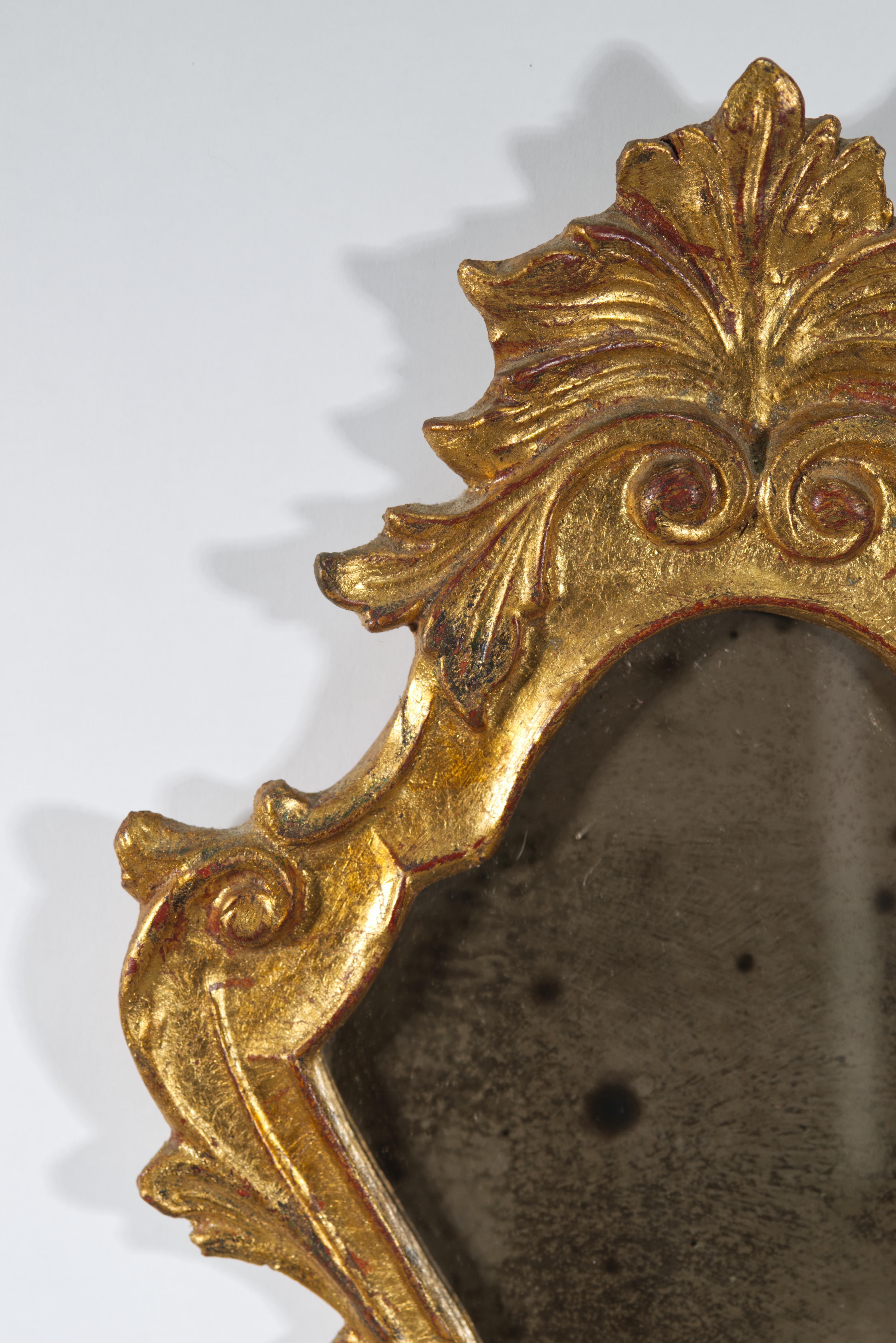 Sculptural vintage Florentine style wall mirror features a highly ornate carved wood and gesso frame with acanthus leaves and scroll details. The frame is decorated with the original gold leaf gilding. Elegant Victorian style frame shows the Rococo