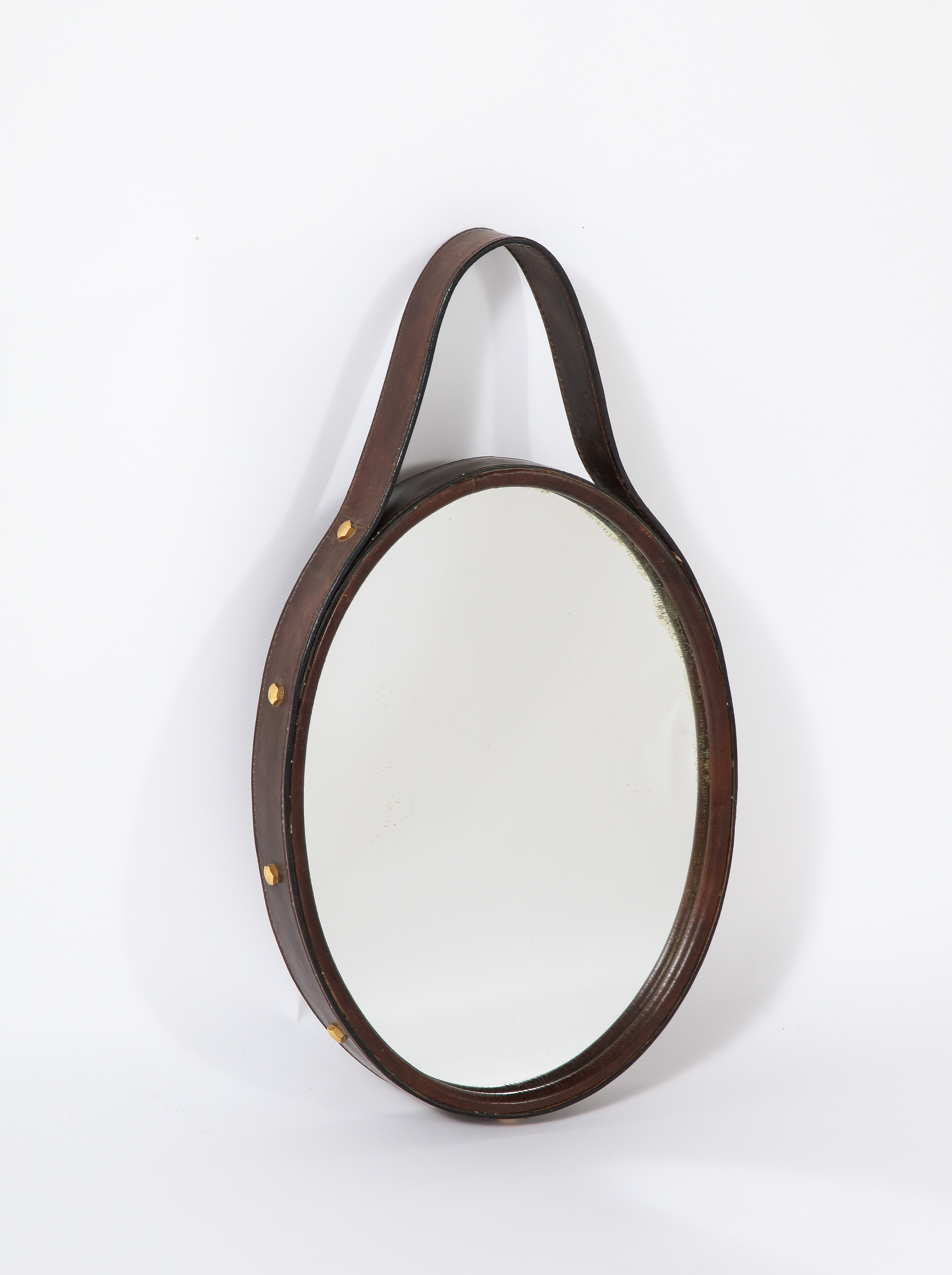 A Florentine 1960's oval framed wood mirror with a thick chocolate brown leather border and handle, the sides of the leather decorated with brass hexagonal nail heads. A highly unique and interesting wall décor.

Florence, Italy, circa