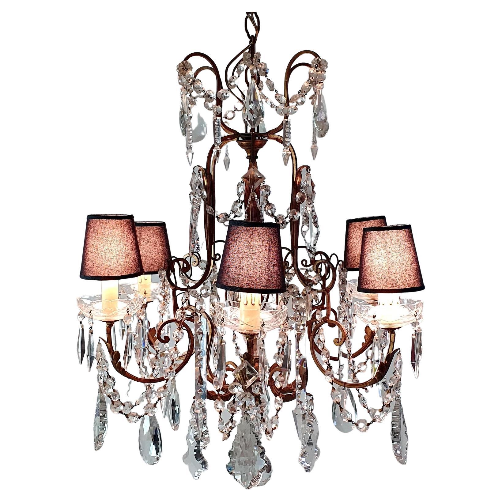 This is a Florentine rococo style chandelier hand made in Florence, Italy circa 1950 with an array of hand made crystals on a guilded iron frame. The chandelier has six candle shaped E14 lights which have been paired with black lampshades which