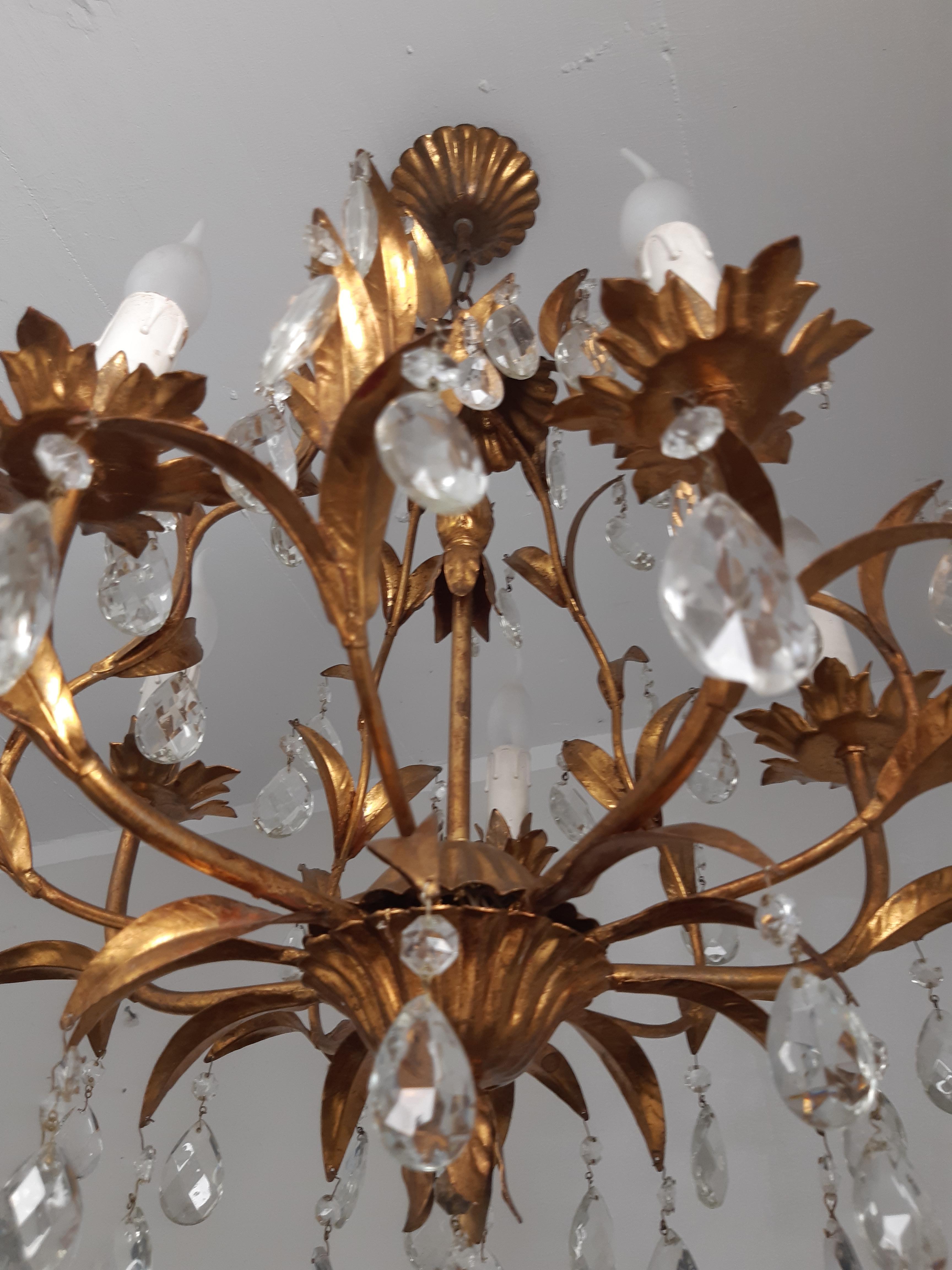 Die elegante Florentiner Deckenleuchte aus den frühen 70er Jahren vereint zeitloses Design und luxuriöse Akzente. Mit ihrem goldfarbenen Metallrahmen und fünf strahlenden Flammen verleiht sie jedem Raum eine warme Atmosphäre. Der kunstvolle