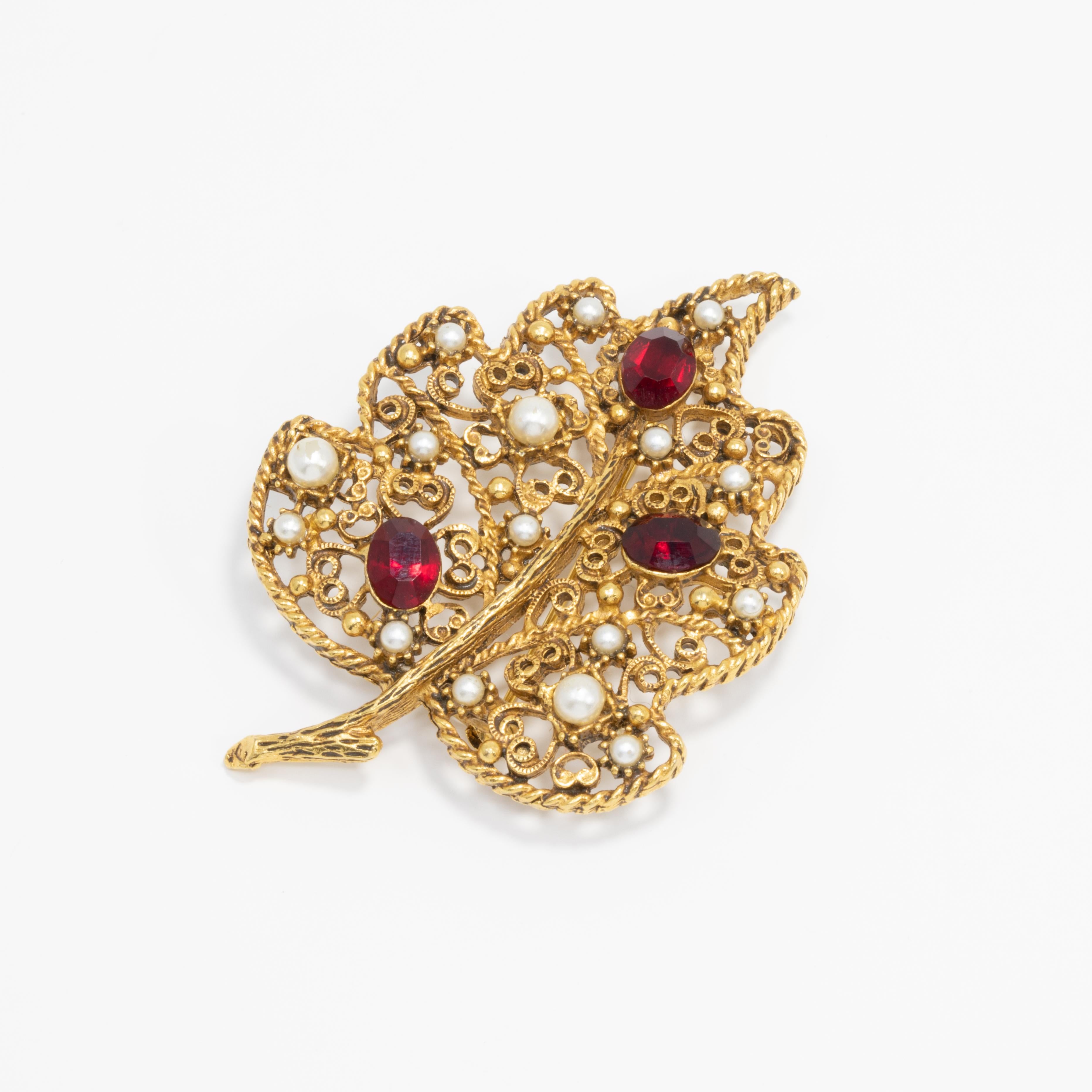 A regal-looking pin brooch by Florenza. This open filigree leaf is decorated with ruby-red crystals and faux pearls.

Gold-tone. Circa mid 1900s.

Hallmarks: Florenza