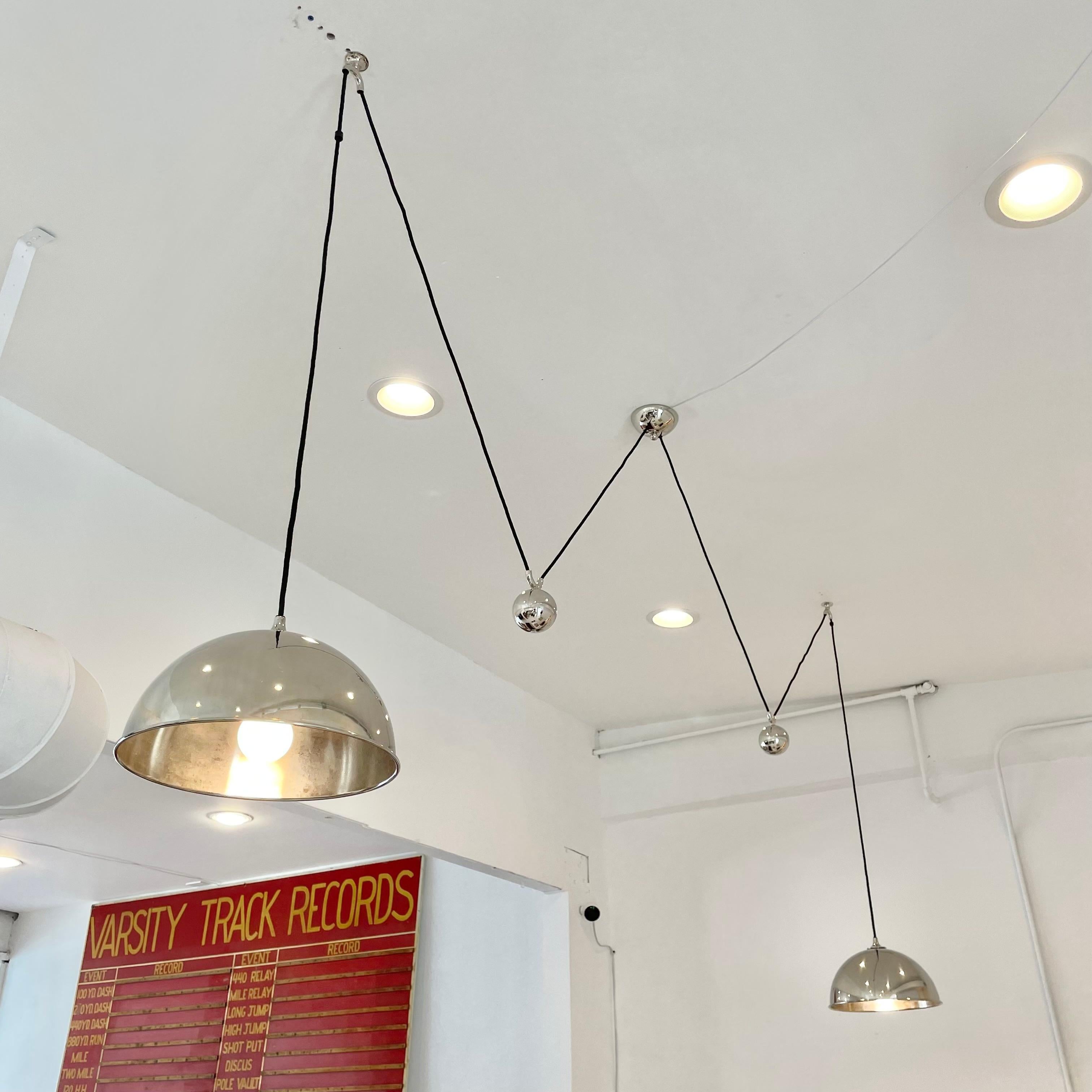 Architectural chrome counter balance chandelier by Florian Schulz. Two chrome pendants hang on both sides of a center canopy. Solid chrome counter weights, canopy and hardware. Black cloth cord. Pendants are height adjustable simply by pulling down