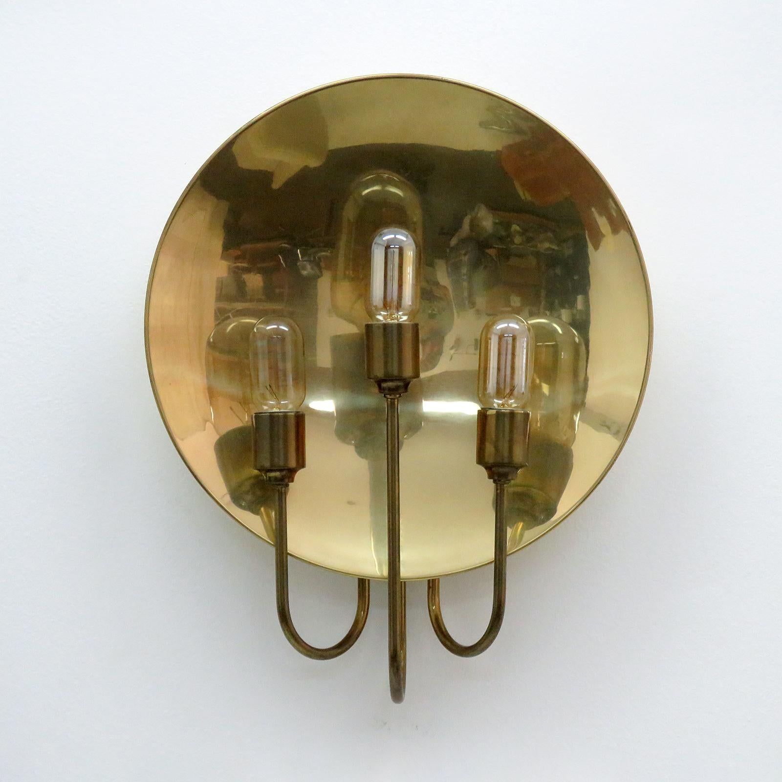 meravigliosa applique a 3 bracci in ottone disegnata da Florian Schulz, Germania, 1960 con tre sorgenti luminose davanti a un riflettore circolare in ottone, cablata per gli standard statunitensi, tre prese E27, potenza massima 60w ciascuna o