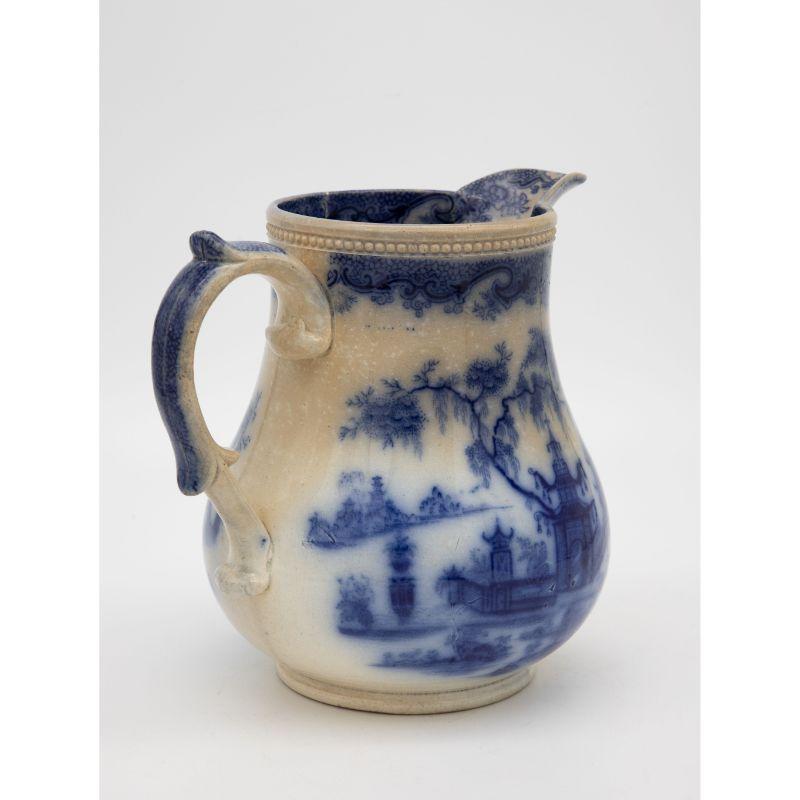 A. English mid 19th C. large Victorian blue and white jug or pitcher decorated with Chinese landscape scenes featuring pagodas and a bridge over water. A decorative handle and spout with a beaded rim.