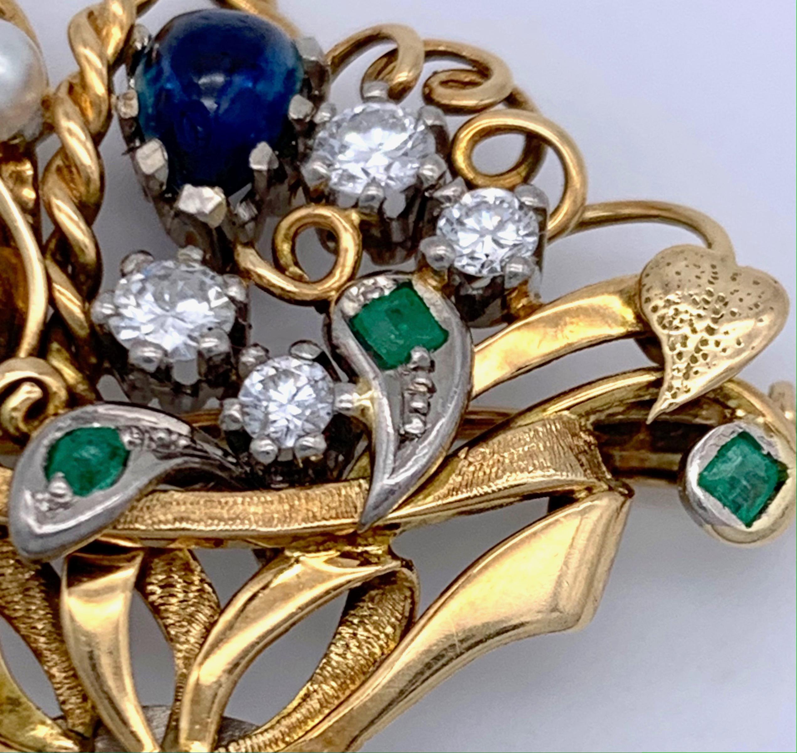 This charming little flower basket is filled with flowers set with 7 diamonds ranging from 0.05 to 0.20 ct. One flower is set with a heart shaped sapphire cabochon, three leaves are set with emeralds. The basket is partially engraved, the handle is