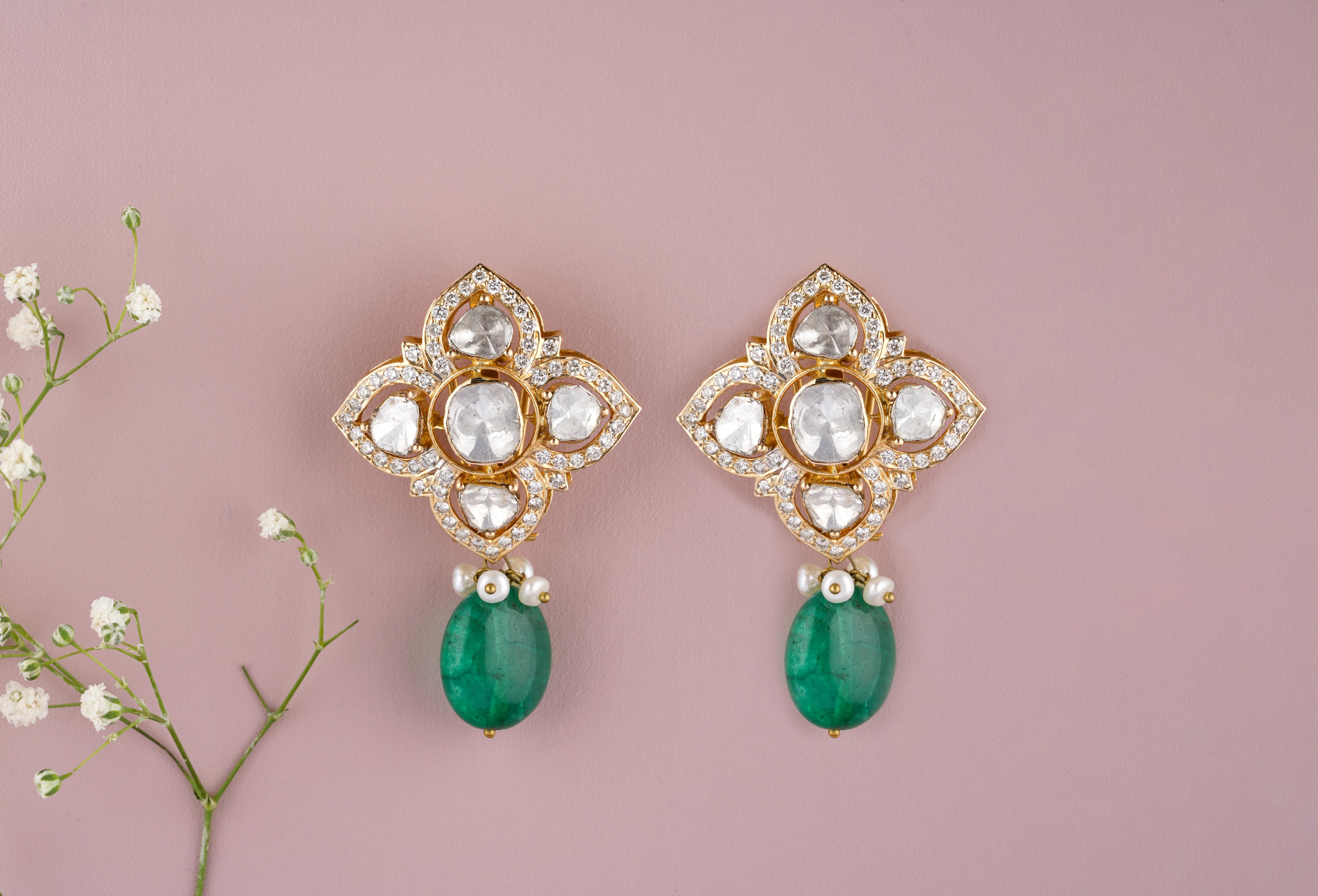 Polki diamond earrings with emeralds are a type of traditional Indian jewelry that feature uncut or raw diamonds (known as Polki) and lush green emeralds. The emeralds provide a pop of color and contrast to the diamonds, making for a stunning and