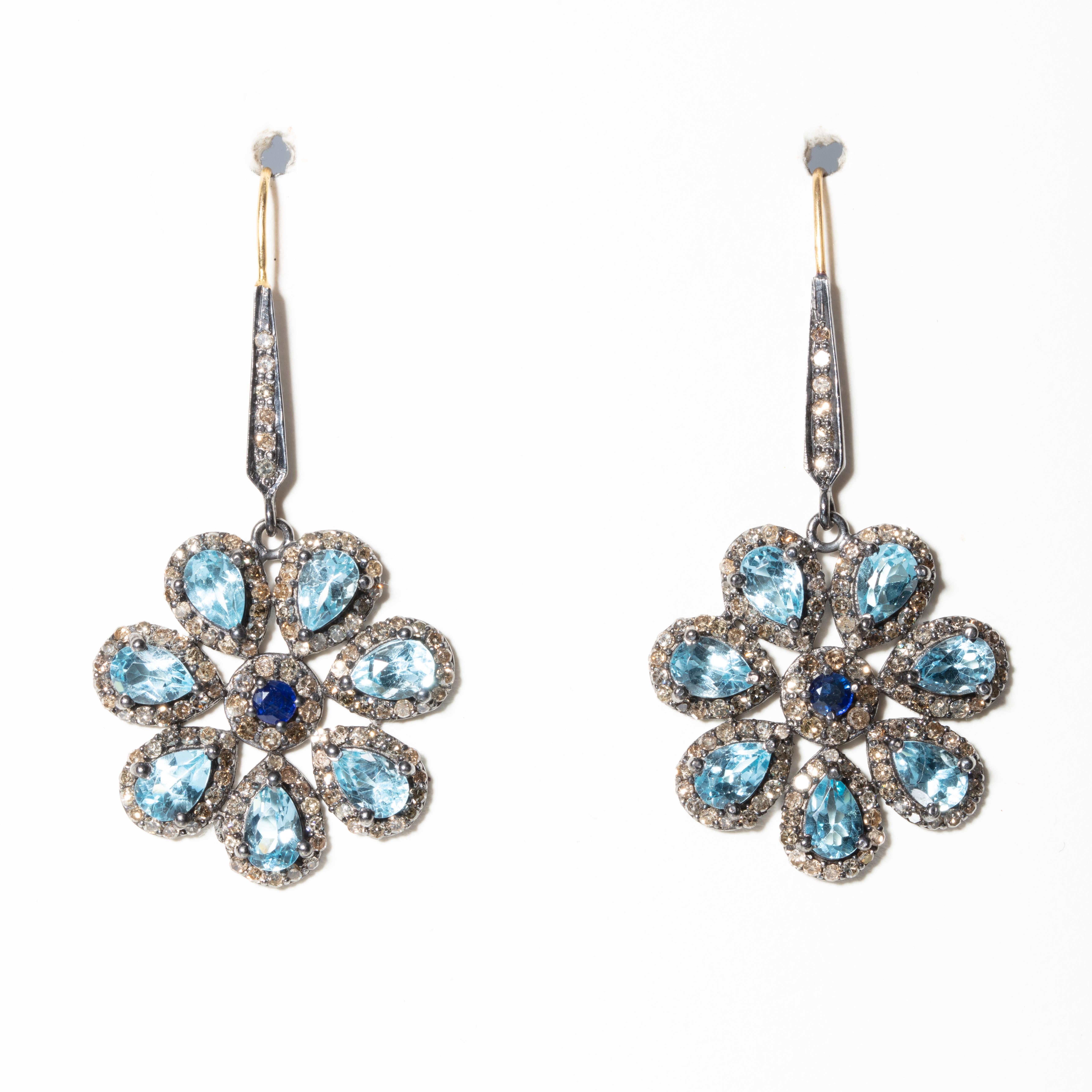 7 petal flower earrings in pear-shaped faceted blue topaz with a faceted center sapphire.  All are surrounded by pave`-set diamonds, and diamonds on the earring wire as well. Set in oxidized sterling with an 18K Gold French wire for pierced ears. 