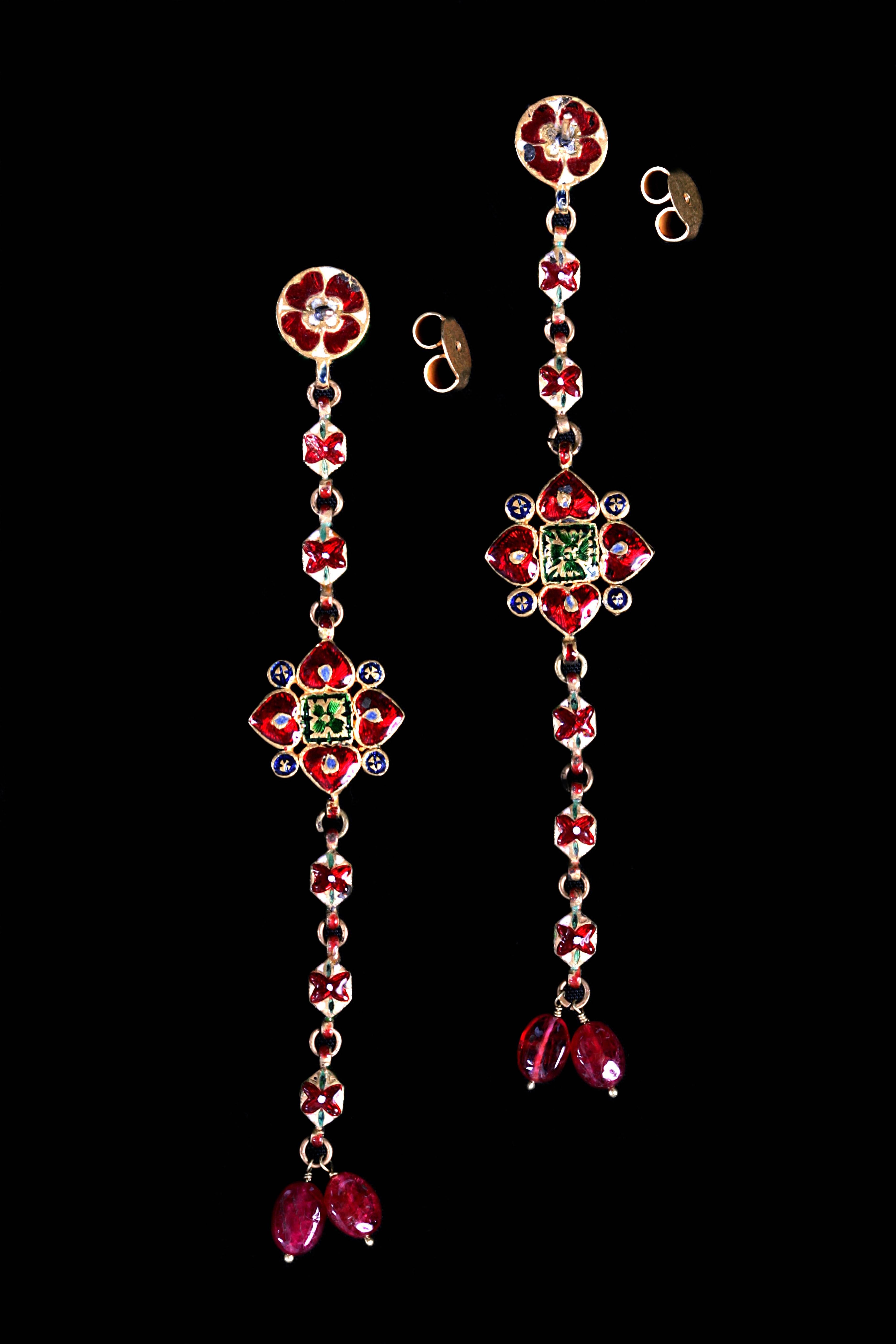 Very delicate long and narrow old gold earrings with small diamonds. A flower in the middle with a ruby in the center. Two hanging spinels on the bottom and a beautiful work of enamel on the back.