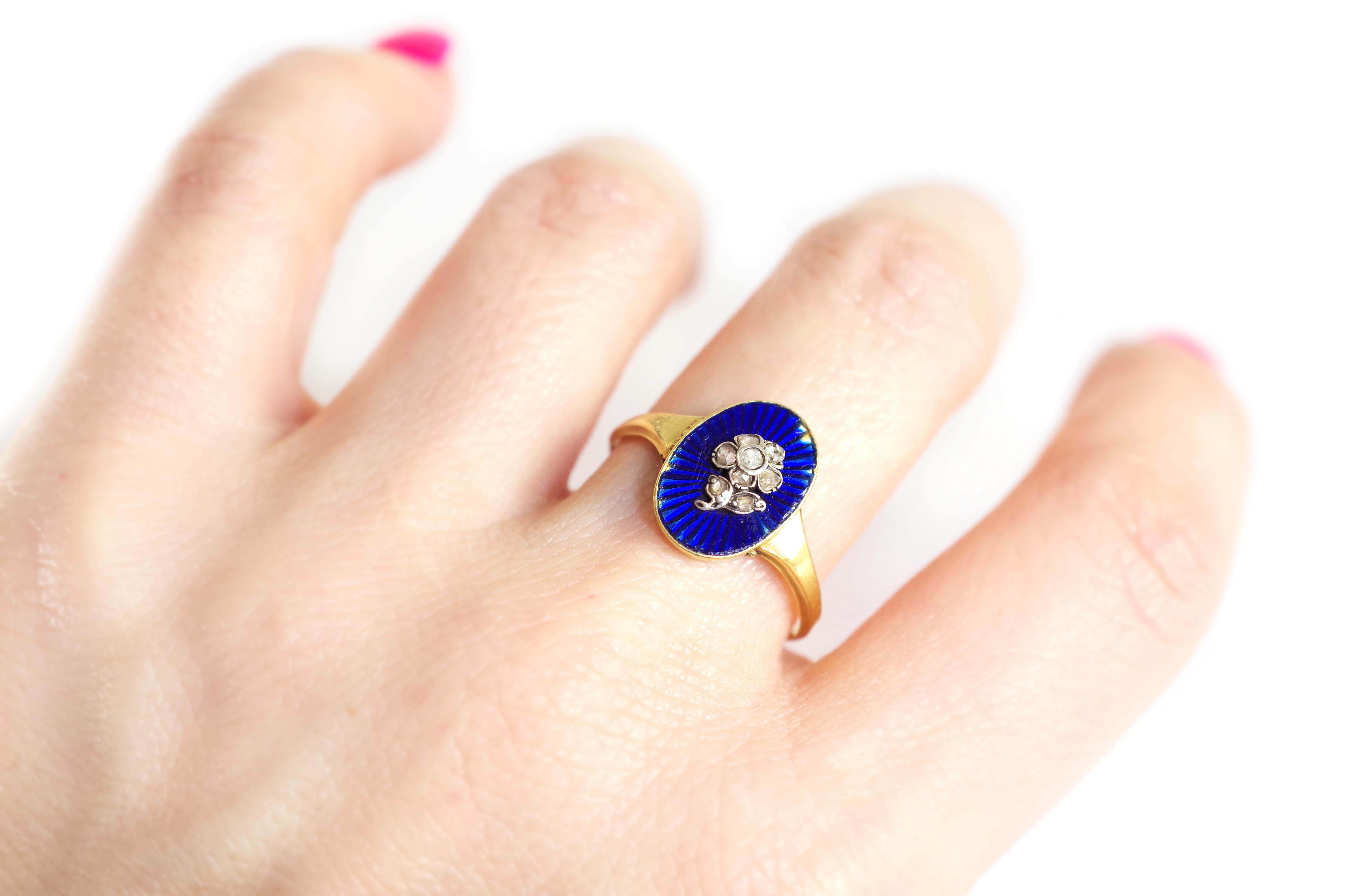 Flower enamel secret locket ring in 18 karat yellow gold. Antique ring with an oval bezel in blue enamelled guilloché on which is applied a silver flower set with eight rose-cut diamonds. A secret compartment is hidden under the bezel, allowing to