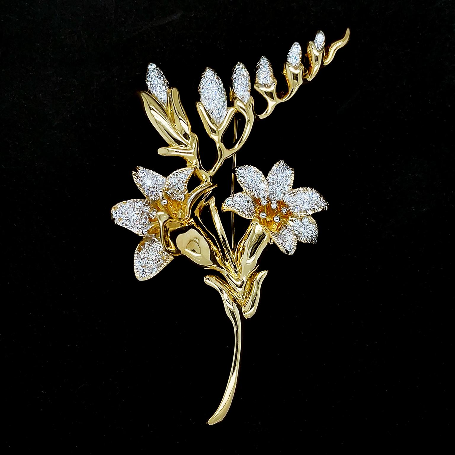 Cette broche s'inspire de fleurs épanouies. L'or jaune 18 carats forme les tiges et les feuilles, tandis que les diamants taille brillant sertis en pavé illustrent les pétales scintillants. Une tige asymétrique en or au-dessus des fleurs présente