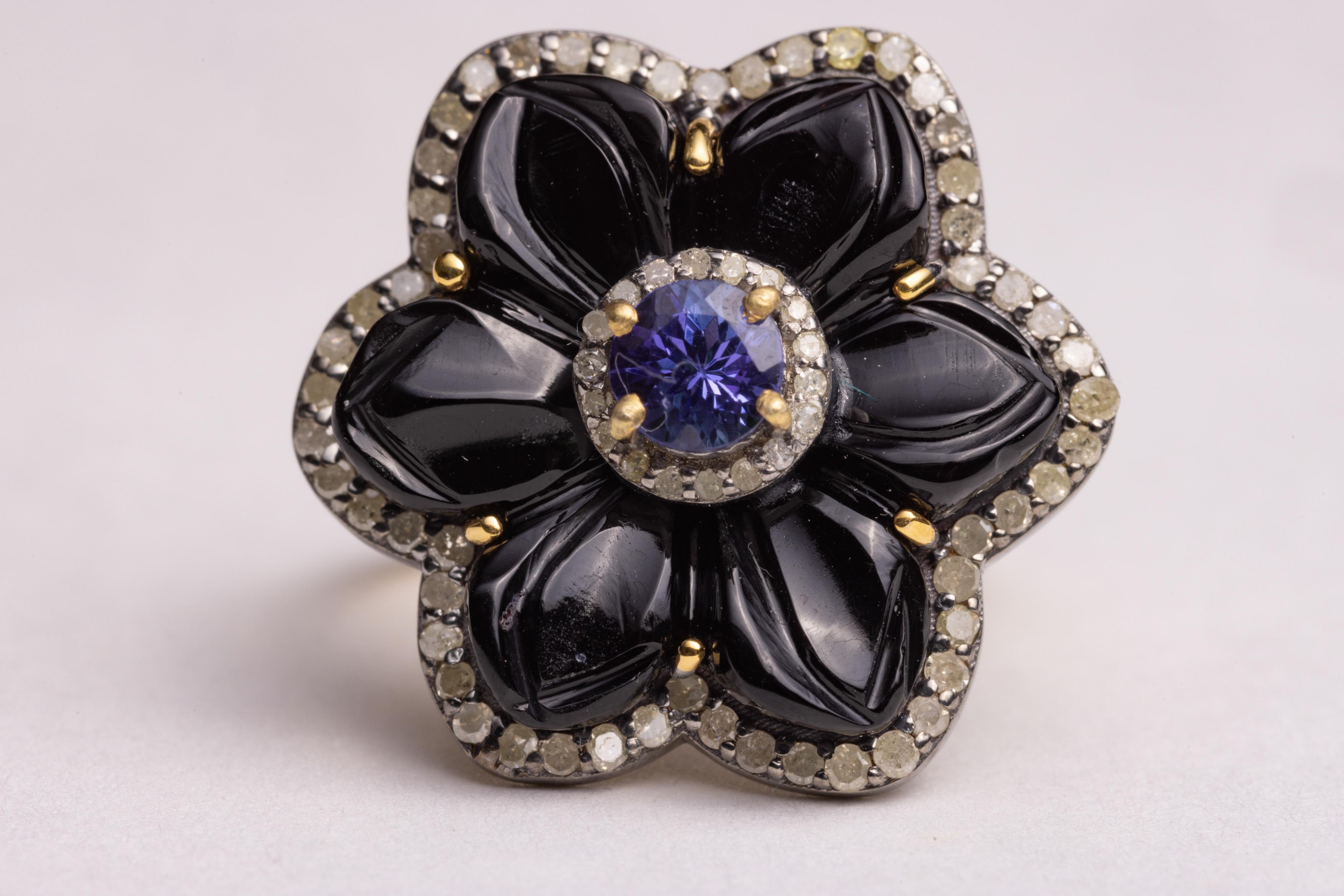 A flower motif cocktail ring in black onyx gemstones carved in the shape of flower petals, bordered with round, brilliant cut diamonds and featuring a round, faceted Tanzanite gemstone in the center. Vermeil 18K gold band.  The diamonds total .61